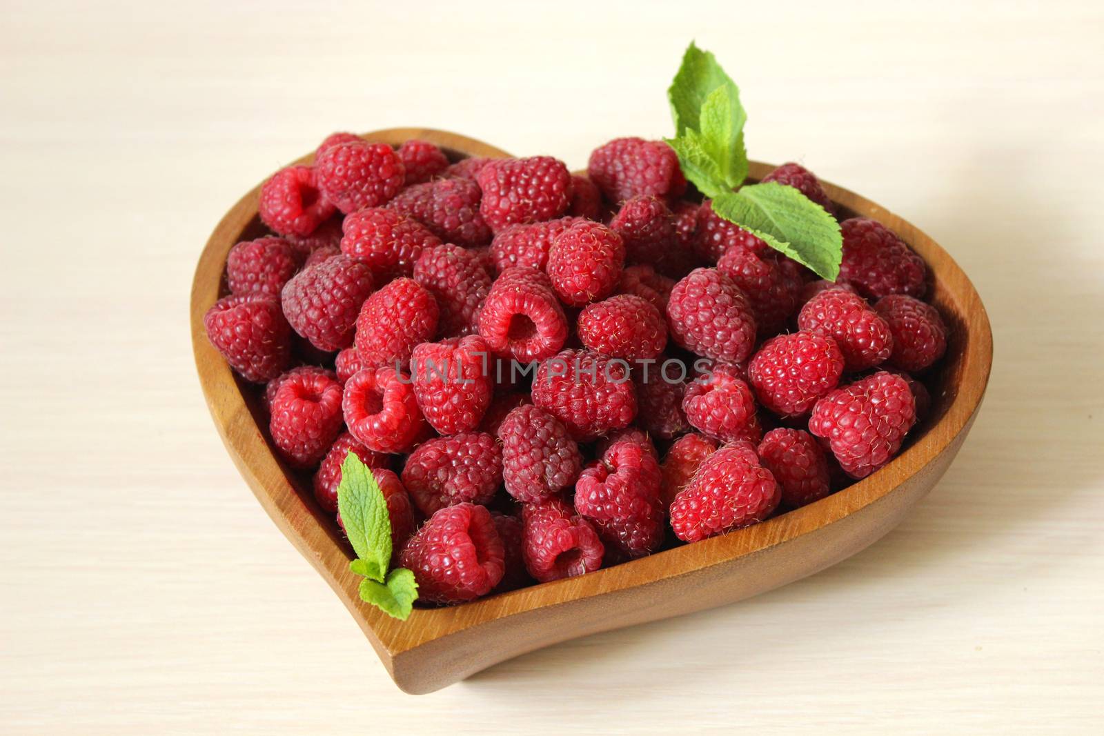 Garden raspberries in a wooden container decorated with a mint leaf on a white background