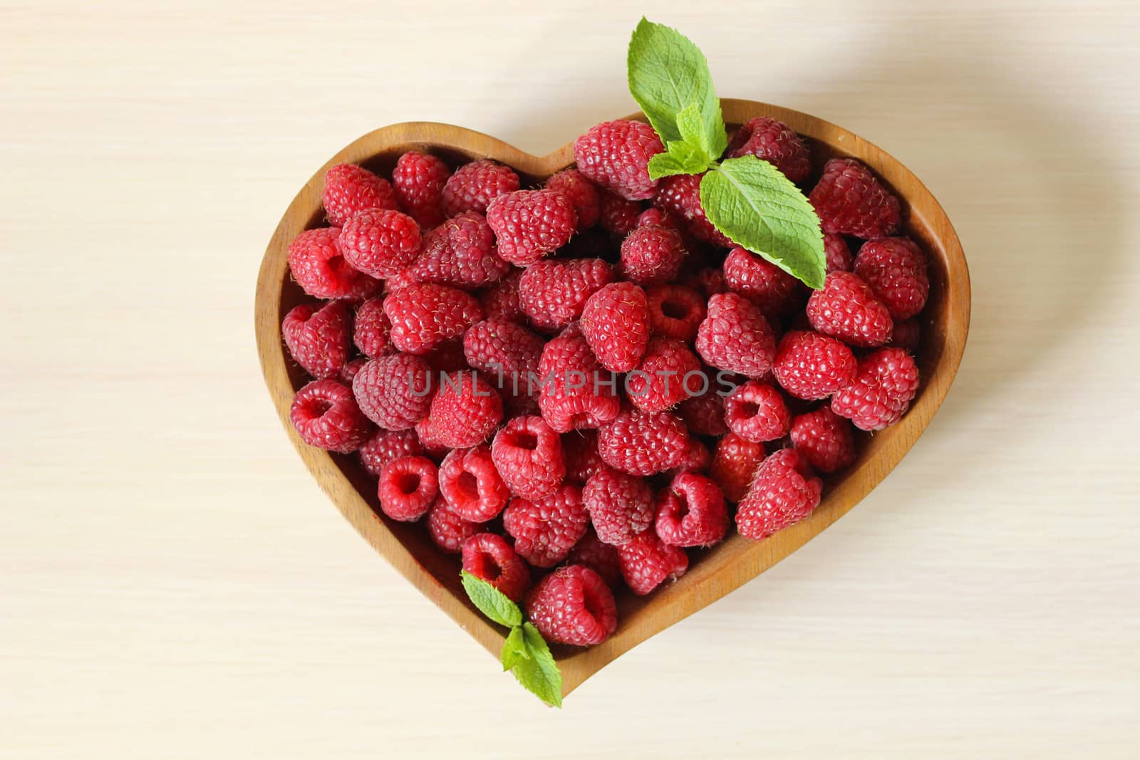 Large raspberries are decorated with a mint leaf on a white background
