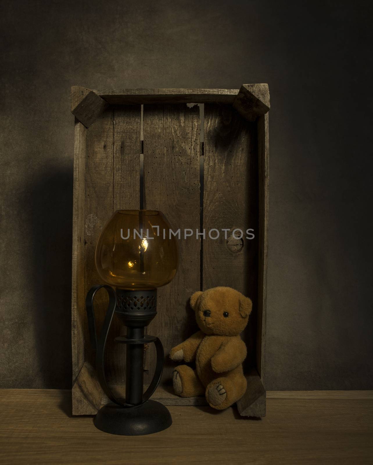 still life with old teddy bear and a golden light in an old wooden box on a table with dark background