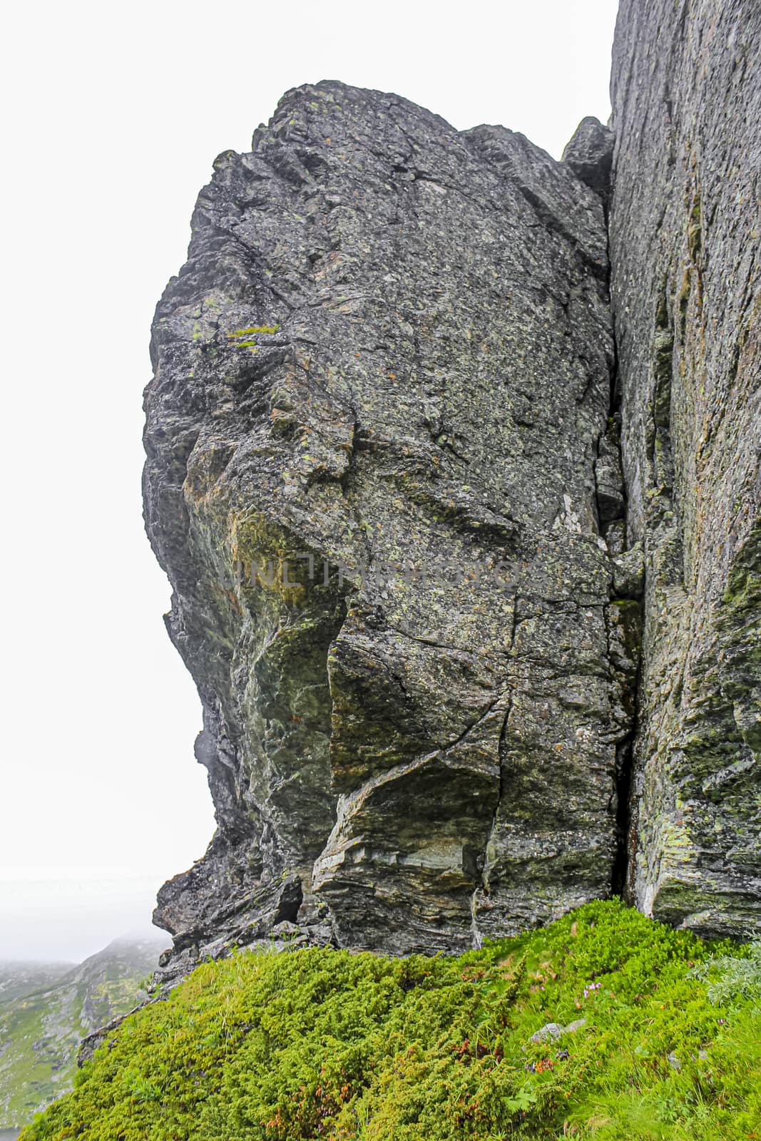 Big rocks cliffs with fog clouds, Veslehødn Veslehorn mountain, Norway. by Arkadij