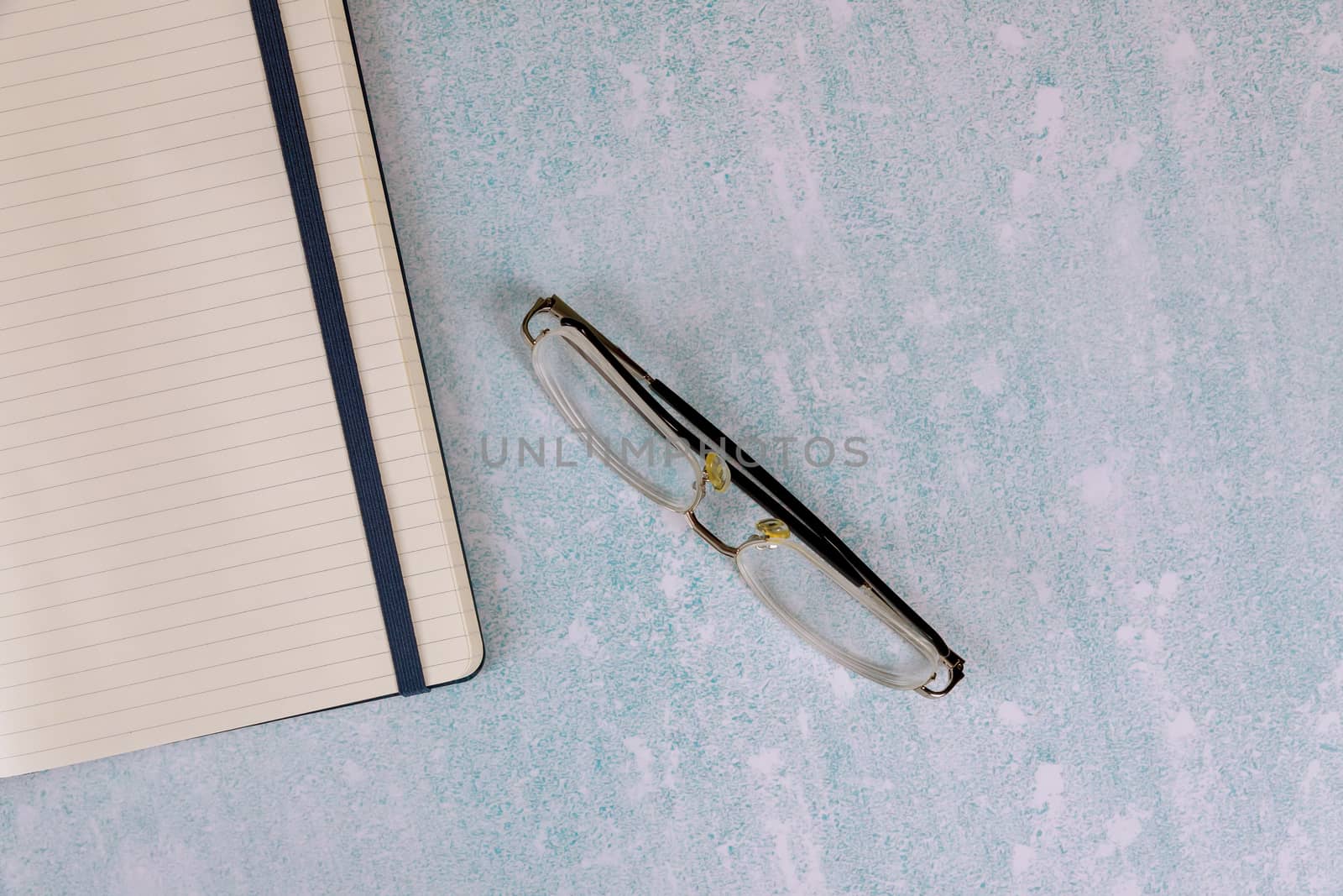 Blank open notepad on eye glasses in office table by ungvar