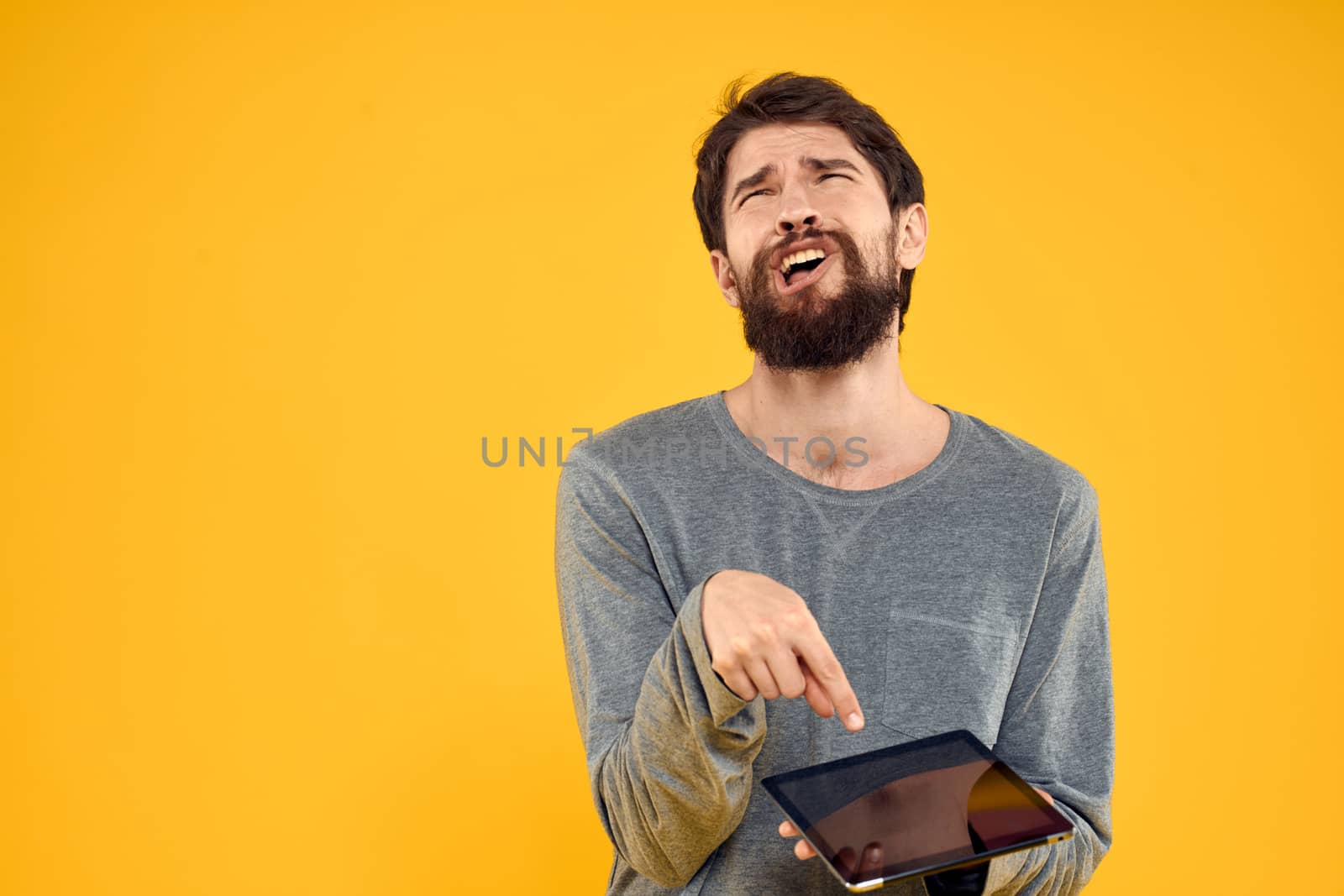 Emotional man with tablet in hands technology internet device lifestyle yellow background. High quality photo