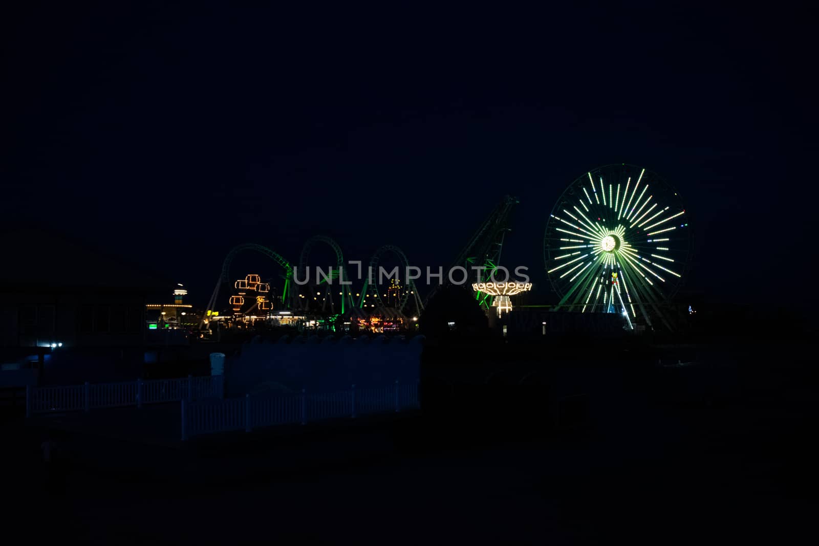 An Amusement Park Pier Lit Up By Lights on the Rides at Night by bju12290