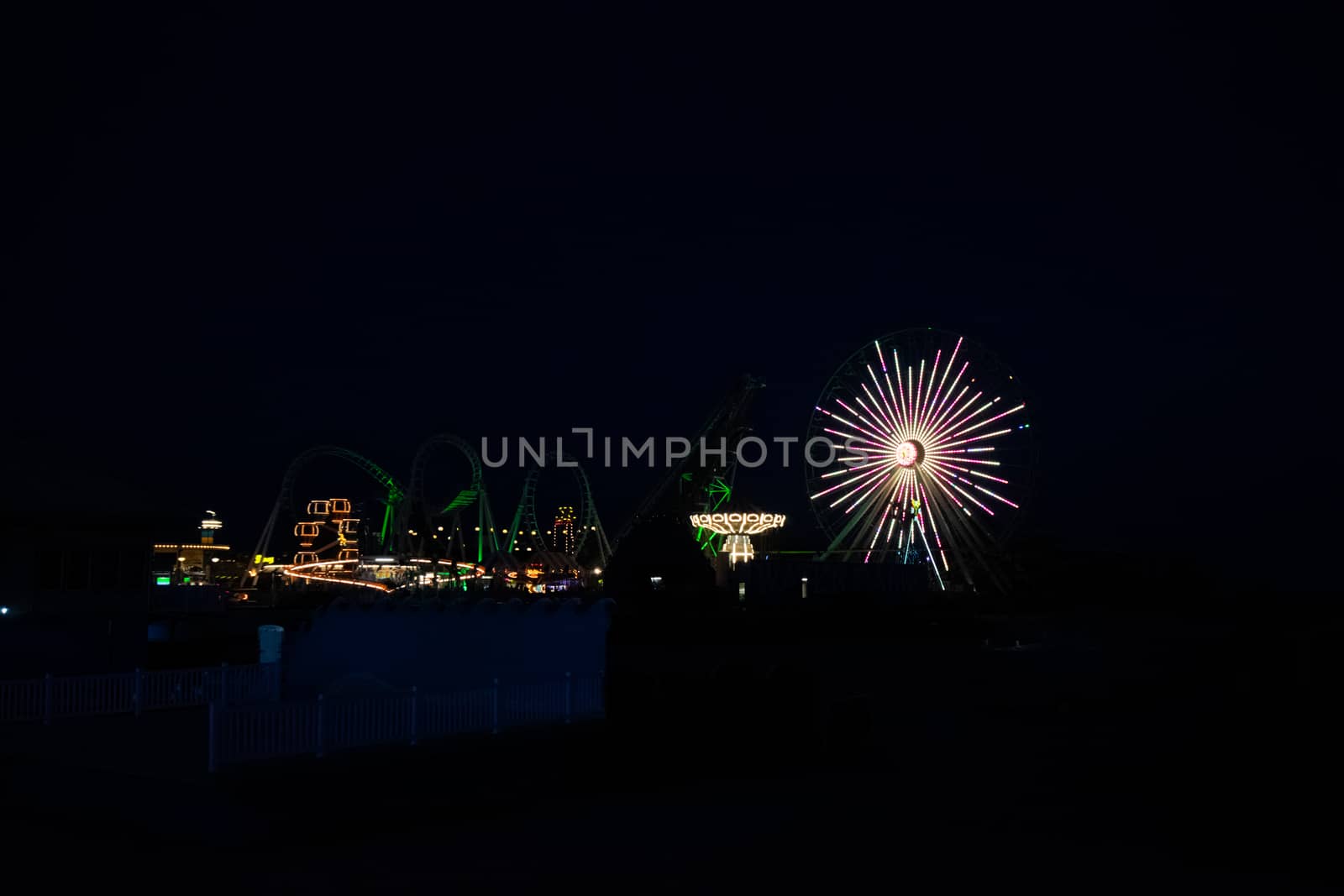 An Amusement Park Pier Lit Up By Lights on the Rides at Night by bju12290