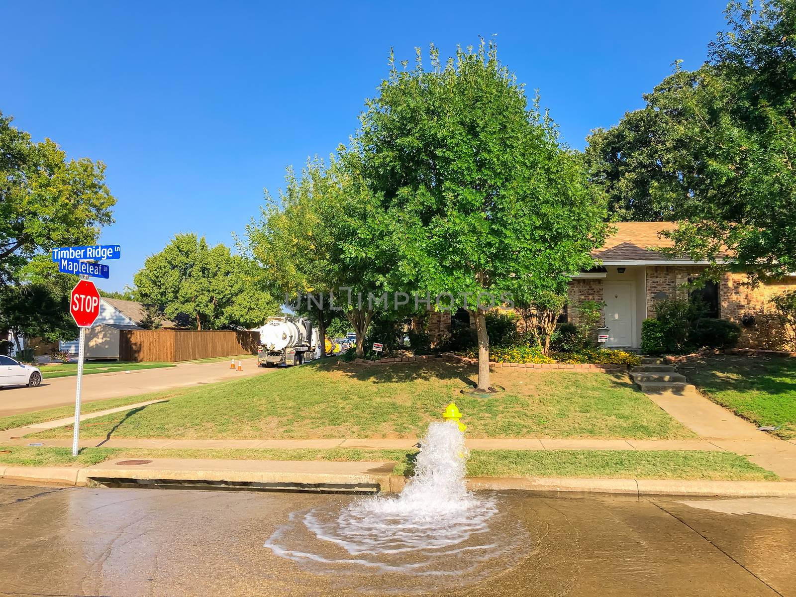 Typical neighborhood area with stop sign near Dallas, Texas, America with open yellow fire hydrant gushing water across a residential street. Row of suburban bungalow single family house behind
