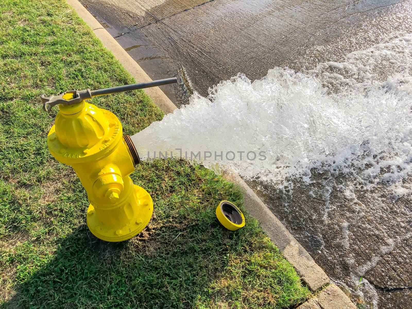 Top view yellow fire hydrant gushing water across a residential street near Dallas, Texas, America. Wide open gushing water to street with grainy effect where water falling back down over the pavement