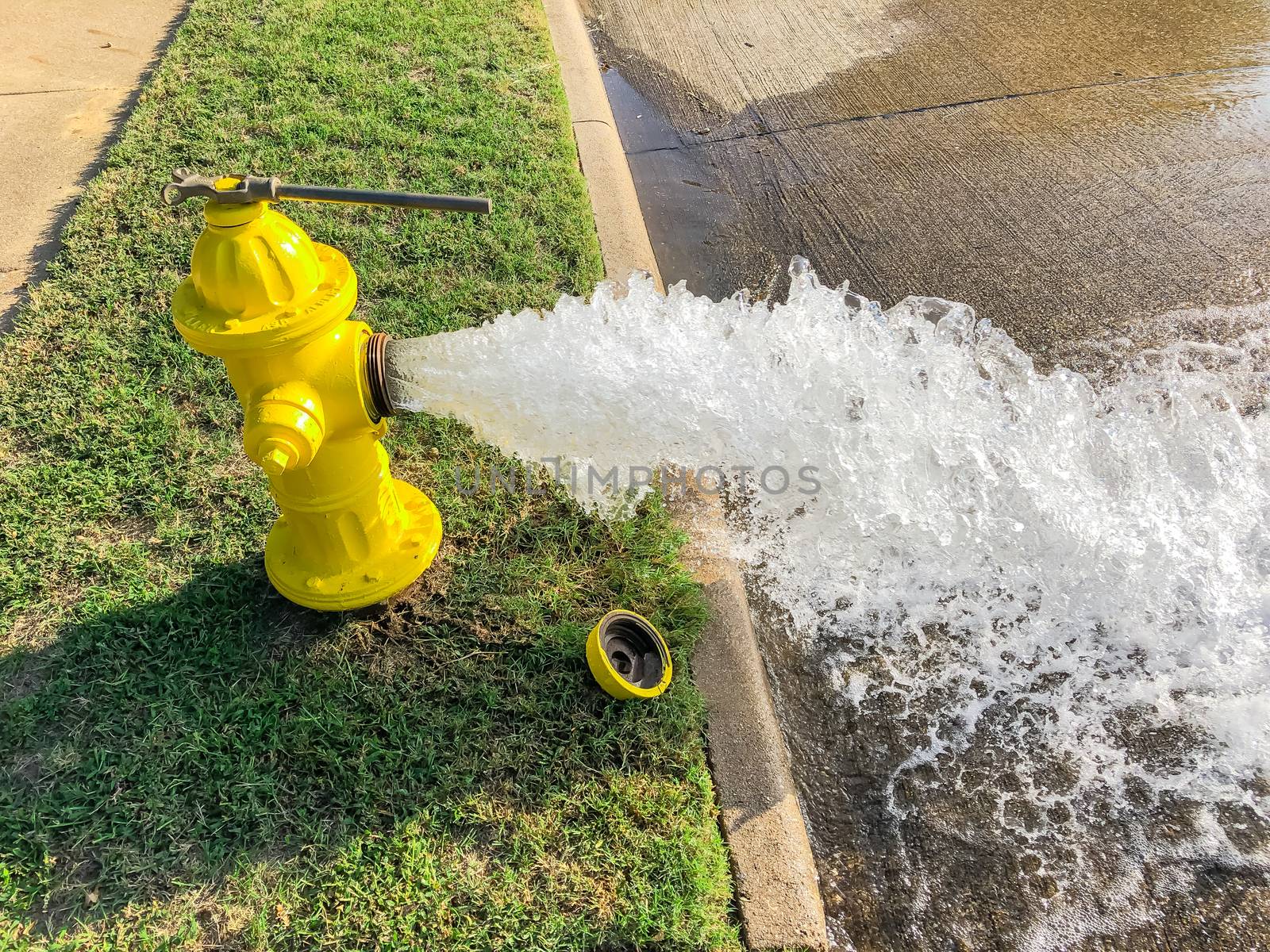 Side view opened yellow fire hydrant gushing water across a residential street near Dallas, Texas, America