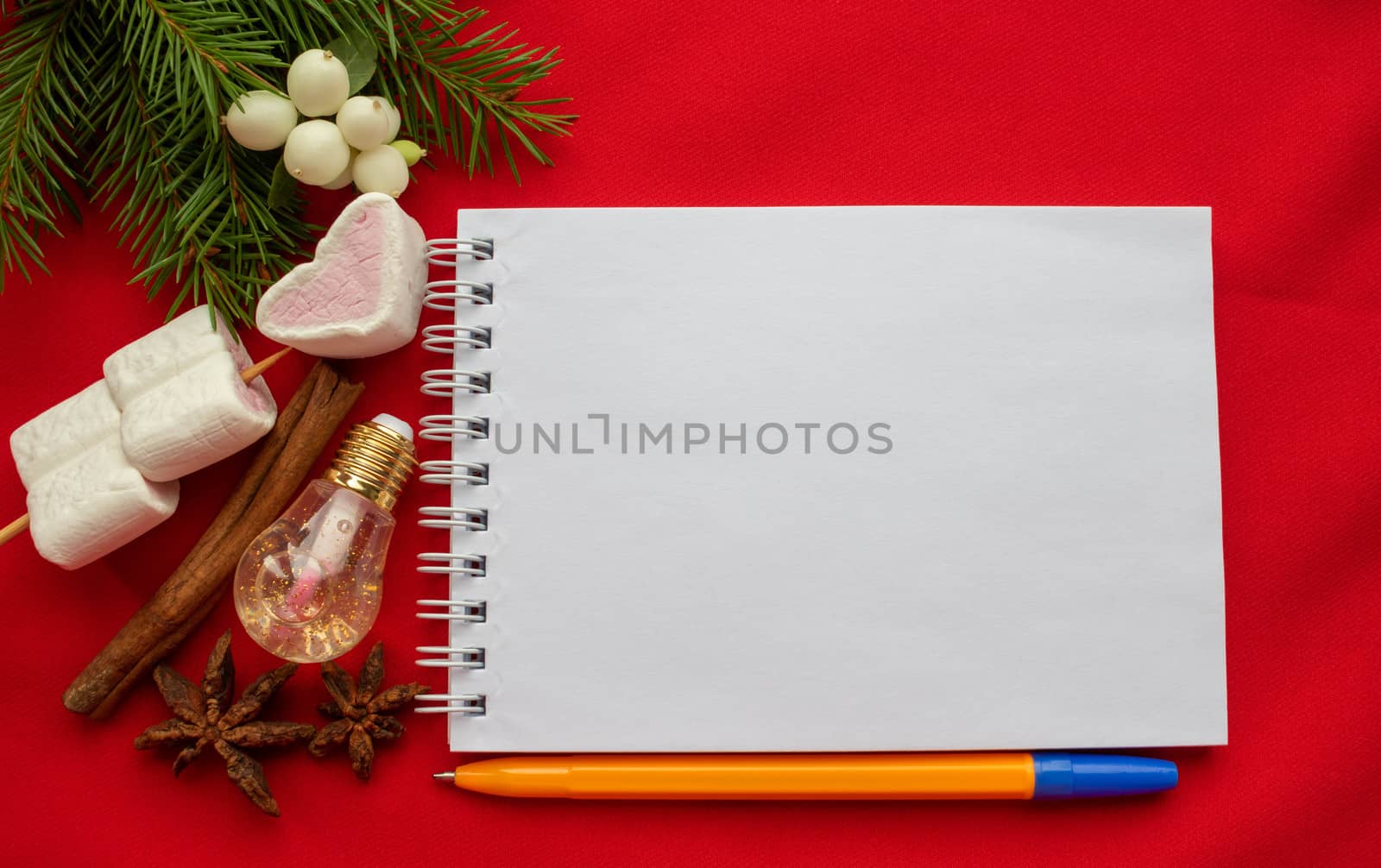 Christmas composition. Notepad and pen, spruce branches, marshmallow hearts,white dogwood berries,cinnamon stick on a red background. Christmas, winter, New year