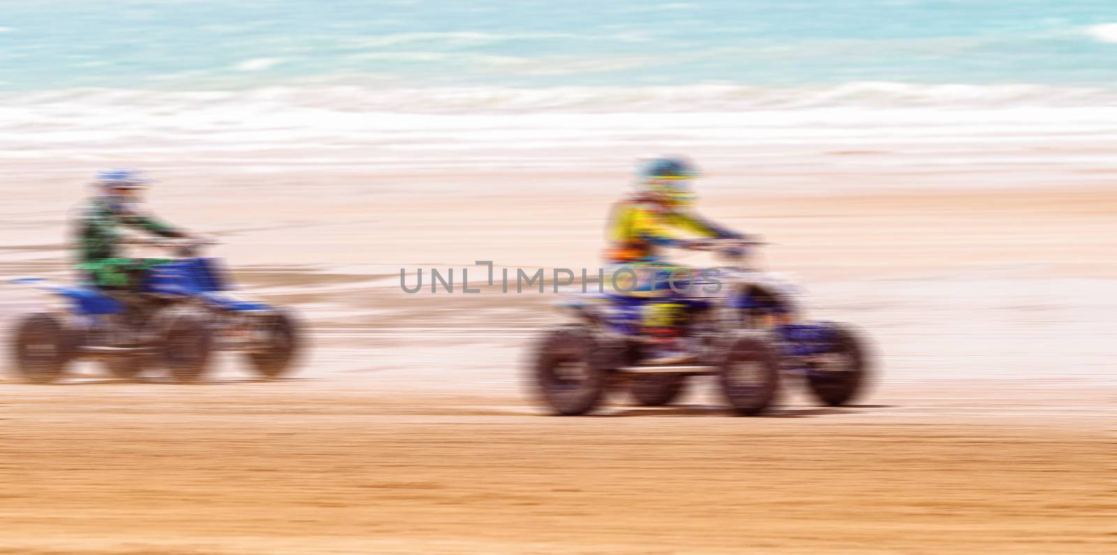 INTENTIONALLY BLURRED BY PANNING TO SHOW THE FAST SPEED MOTION OF Unidentified riders and bikes participating in motorcycle racing on a sandy beach