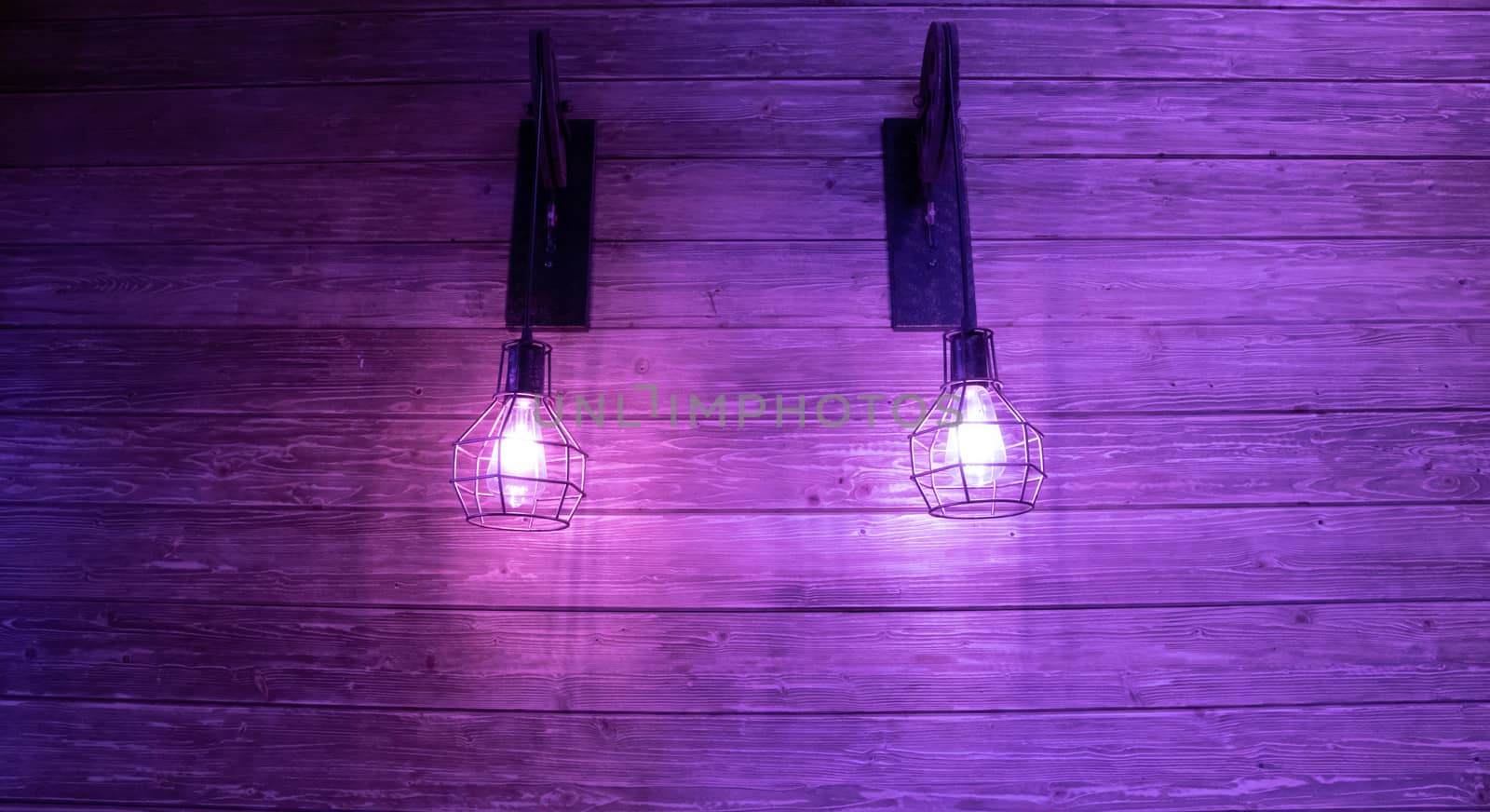 Two antique lamps on a lilac wood wall.