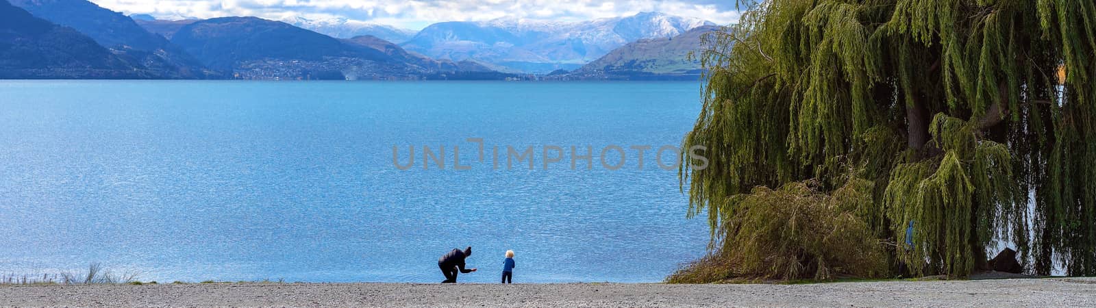 A mother shows her child how to skip stones across a scenic lake