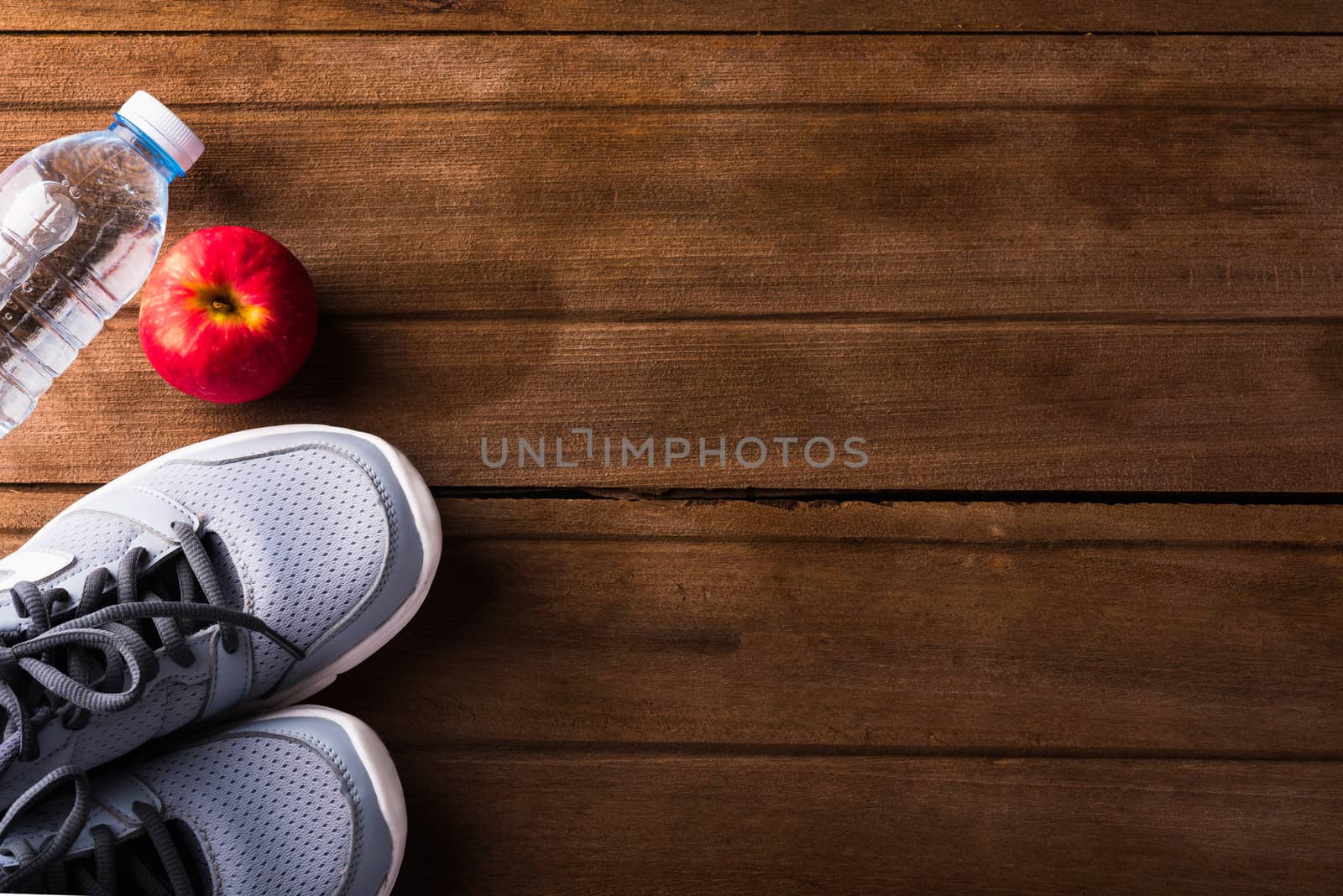 Top view of pair sports shoes, bottle water and red apple on wood table, Gray sneakers and accessories equipment in fitness GYM, Healthy workout concept