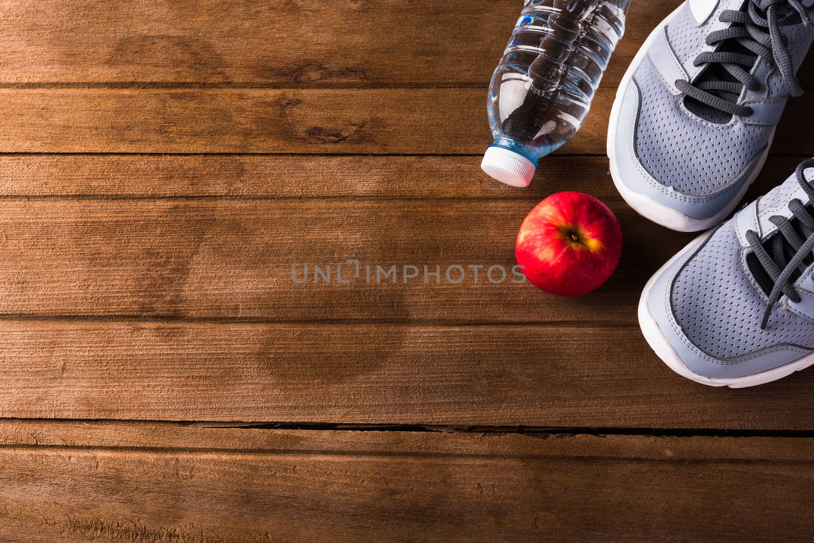 Top view of pair sports shoes, bottle water and red apple on wood table, Gray sneakers and accessories equipment in fitness GYM, Healthy workout concept