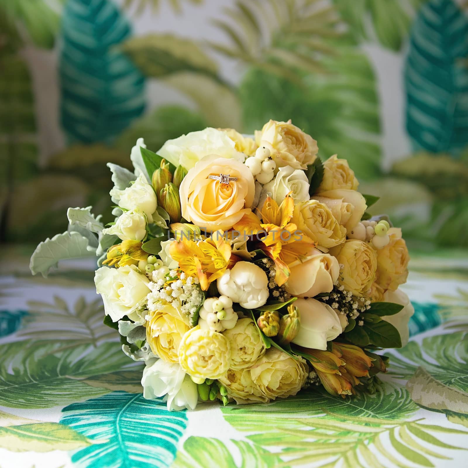 A floral bridal bouquet of yellow blooms against a leafy patterned background