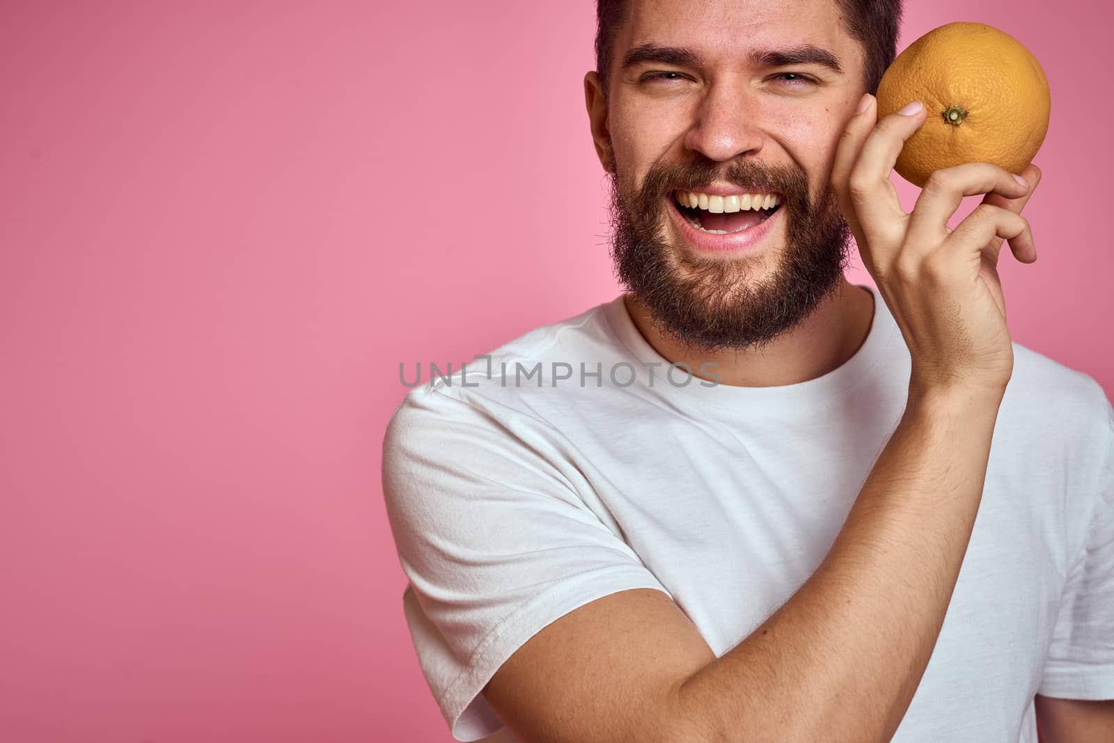 Young man with orange on a pink background in a white t-shirt emotions fun gesticulating with model hands. High quality photo