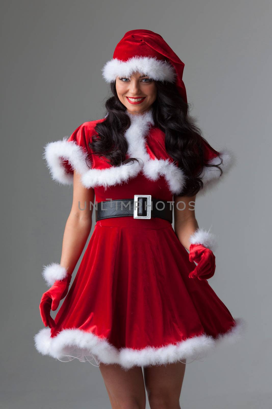 People, holidays, christmas and celebration concept - beautiful sexy woman in santa hat and red dress on gray background
