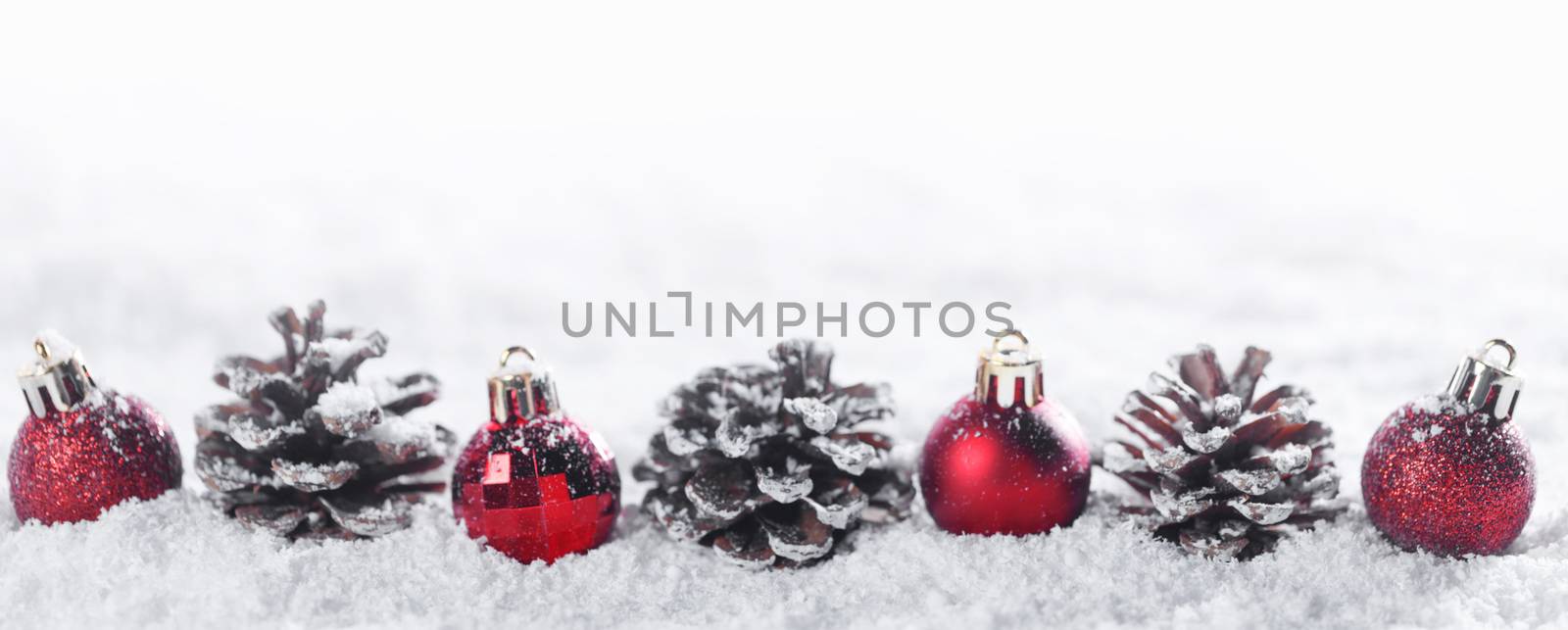 Winter Christmas decor of red christmas bauble ball row and pine cones in snow isolated on white background