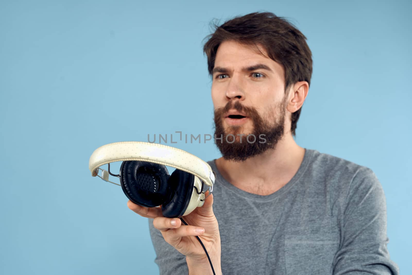 Man with headphones in hands music emotion technology lifestyle fun blue background close-up. High quality photo