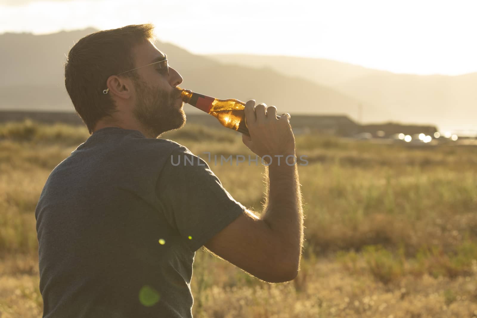 A young man drinks beer from a bottle at sunset, Spain by alvarobueno
