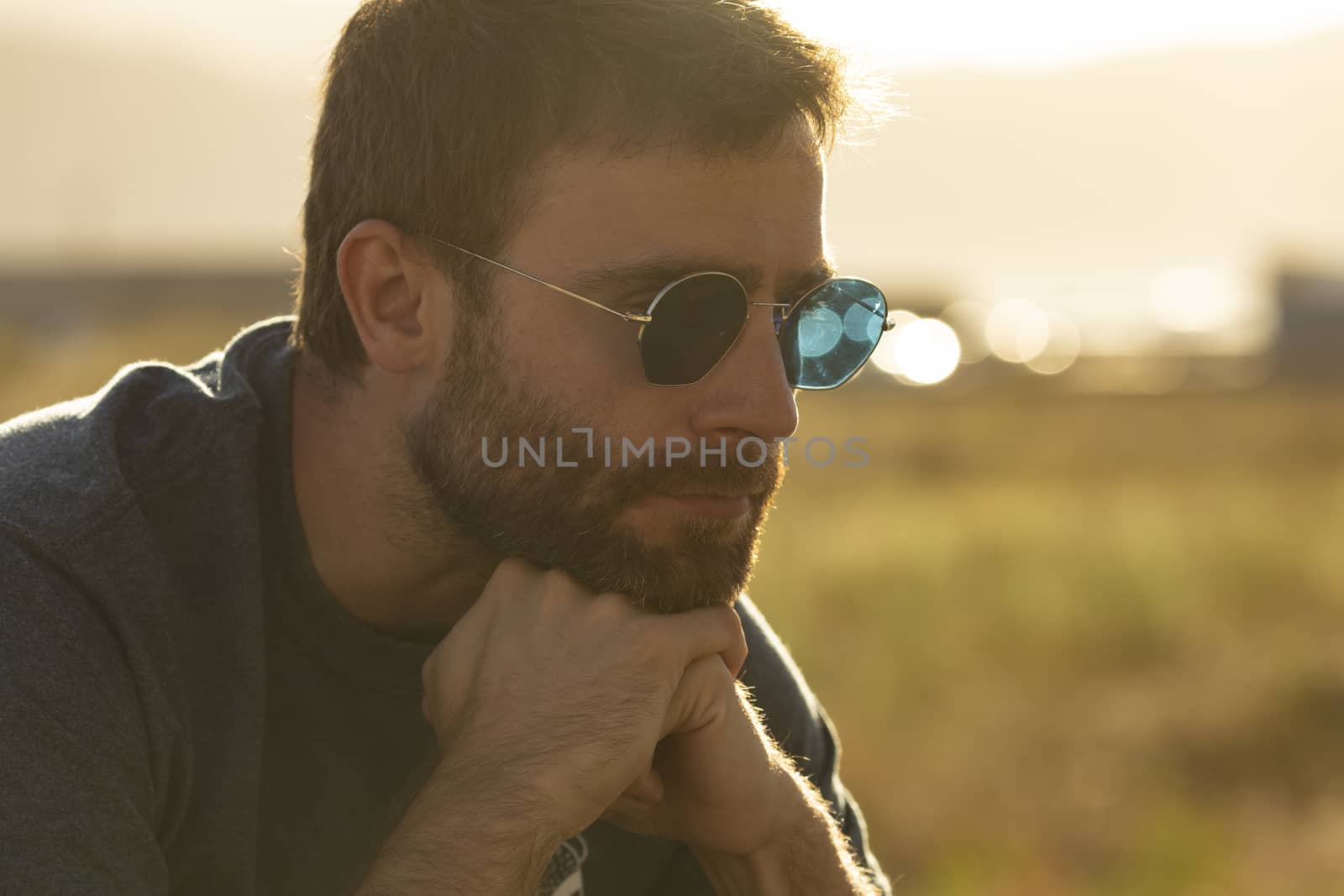 A young man, wearing sunglasses, meditates serenely at sunset. by alvarobueno