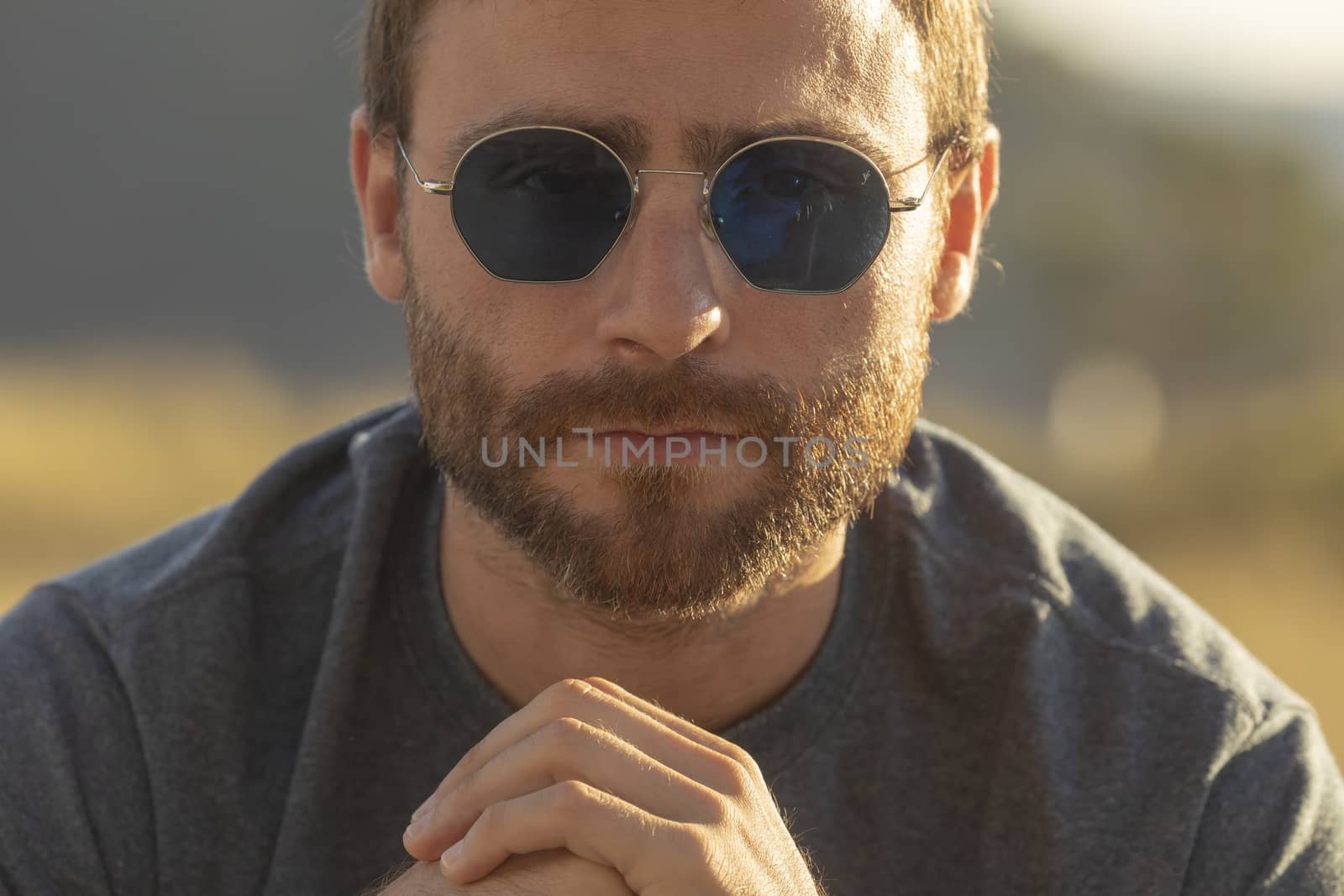 A young man, wearing glasses, concentrating on himself, meditates in a relaxed way, while enjoying the afternoon sun on a promenade in northern Spain.