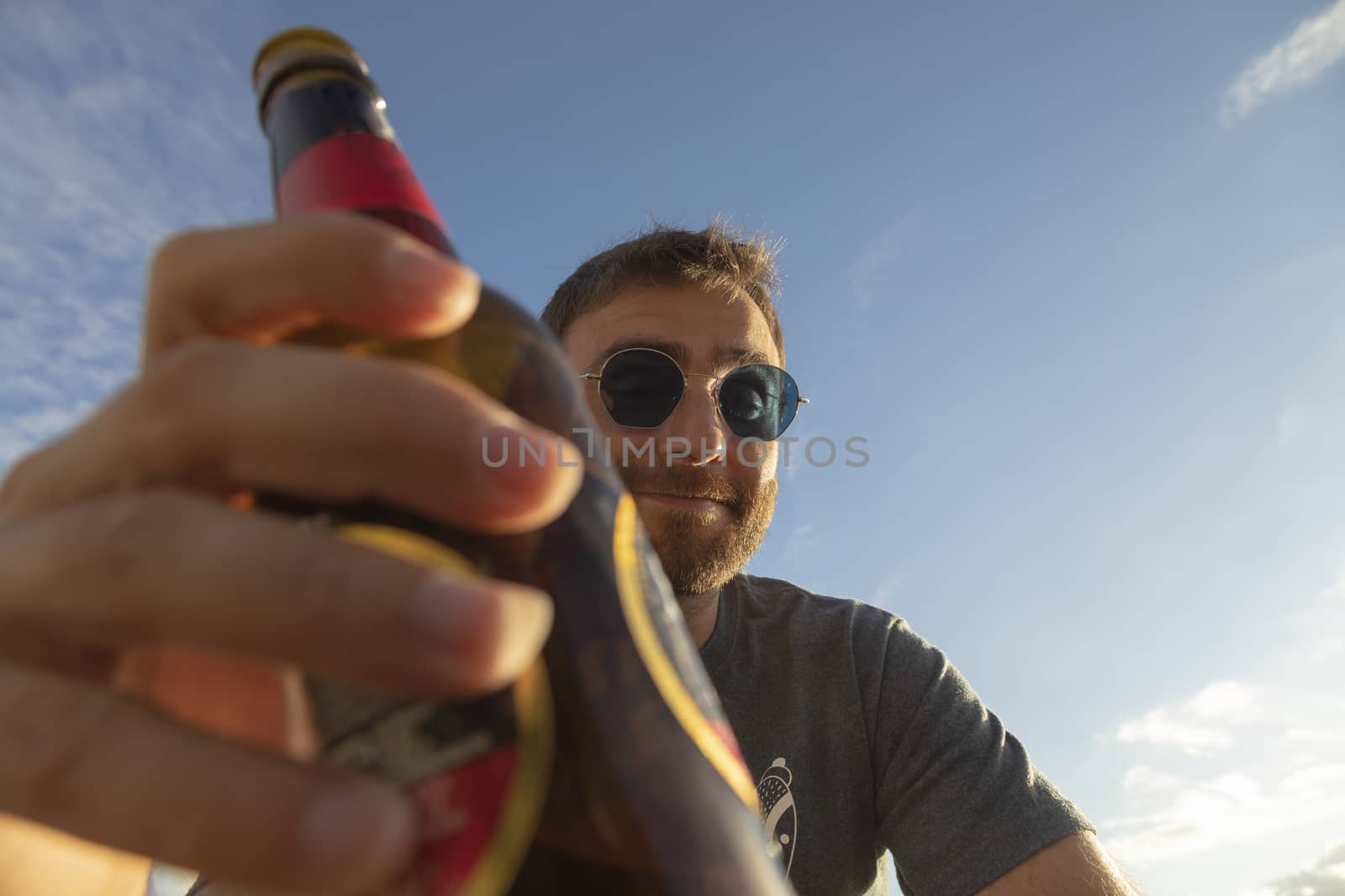 A young man, with glasses, toasts with beer, enjoying the sunset in Galicia, northern Spain.