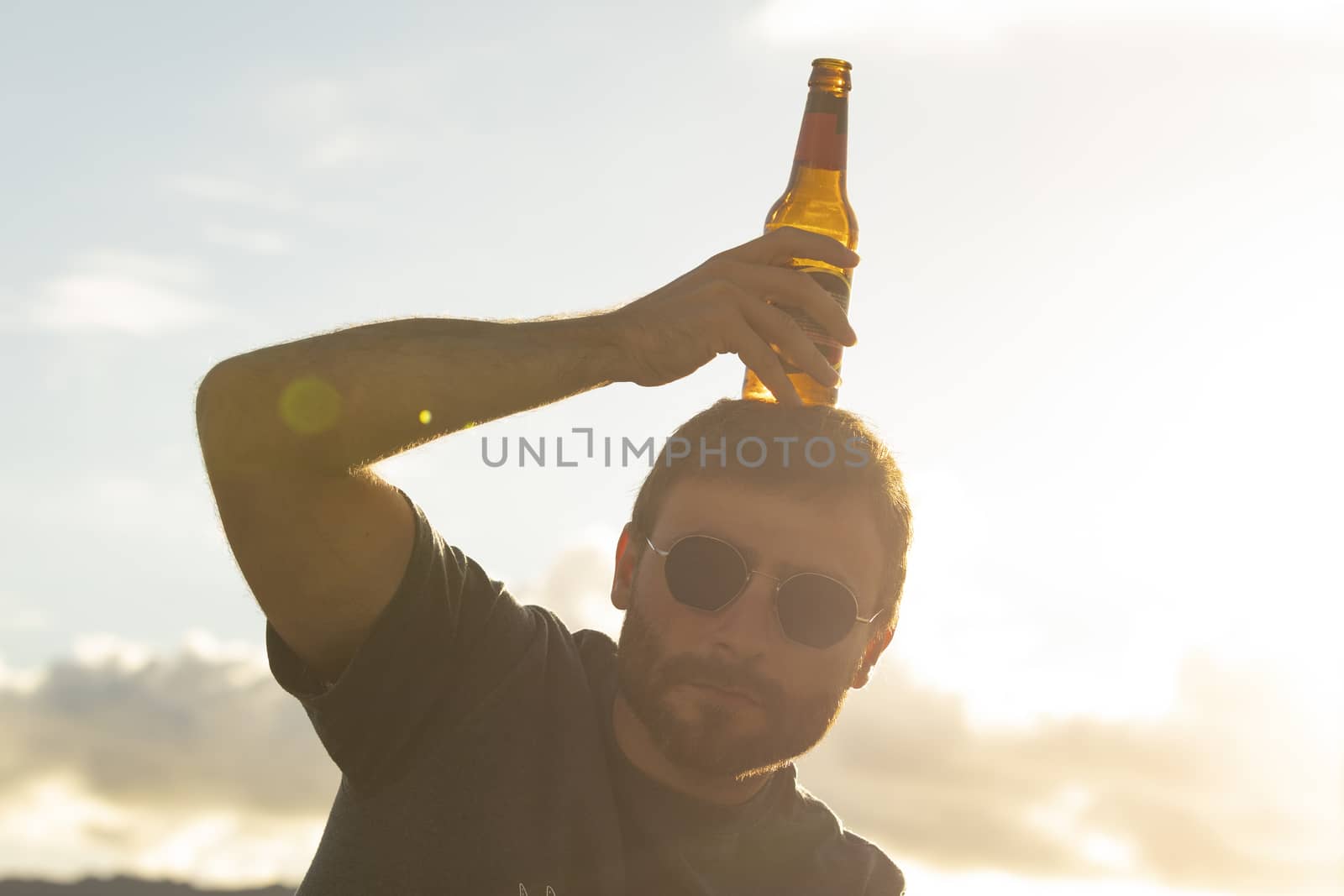 A young man, with glasses, does silly things, while drinking beer from a bottle, enjoying the sunset in Galicia, northern Spain.