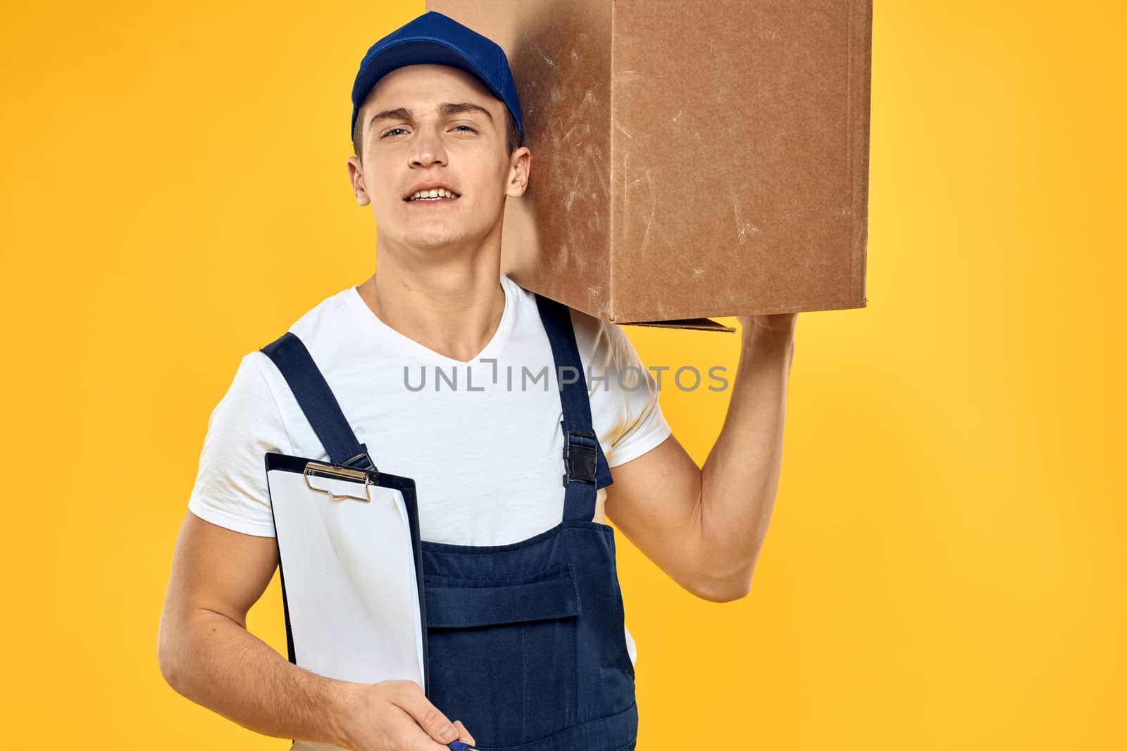 Working man in uniform with box hand delivery loading service yellow background. High quality photo