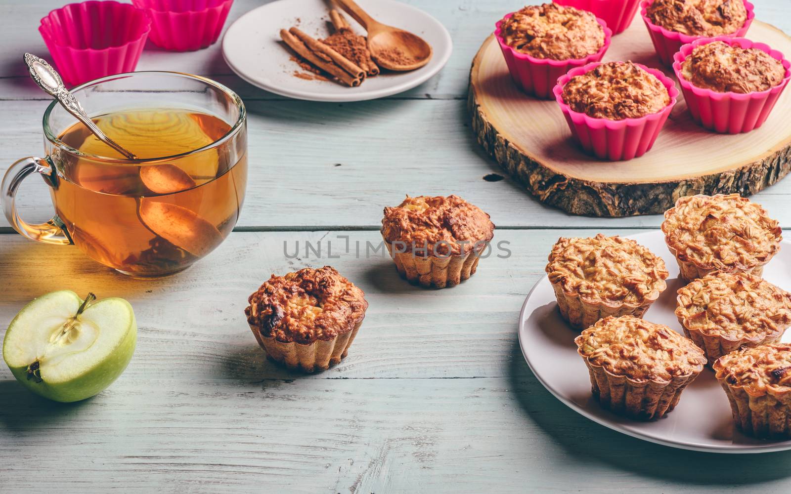 Healthy Breakfast. Cooked oatmeal muffins with apple and cup of green tea over light wooden background.