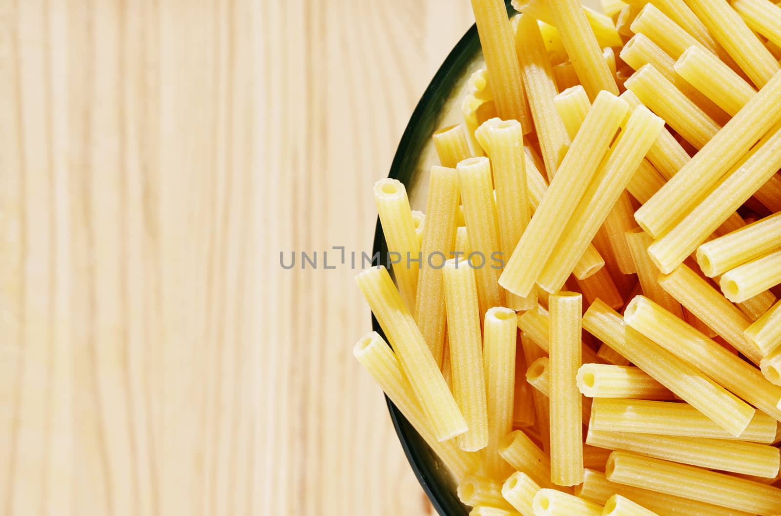 Pile of yellow pasta maccheroni in glass bowl on wooden table , dry pasta shaped like narrow tubes ,