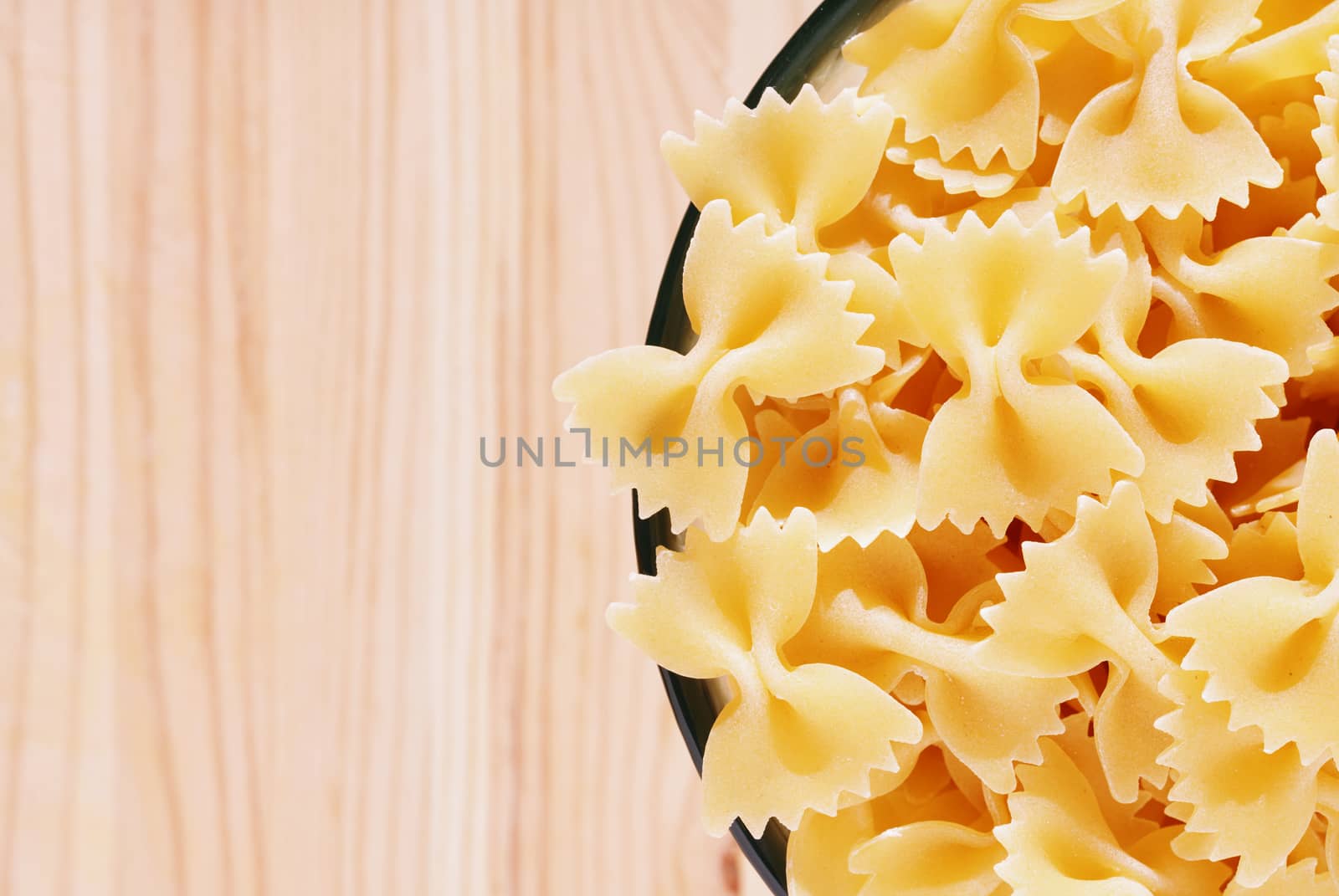 Dry pasta farfalle in glass bowl on wooden table , bow-tie pasta or butterfly pasta with two ruffled edges and the centre pinched together