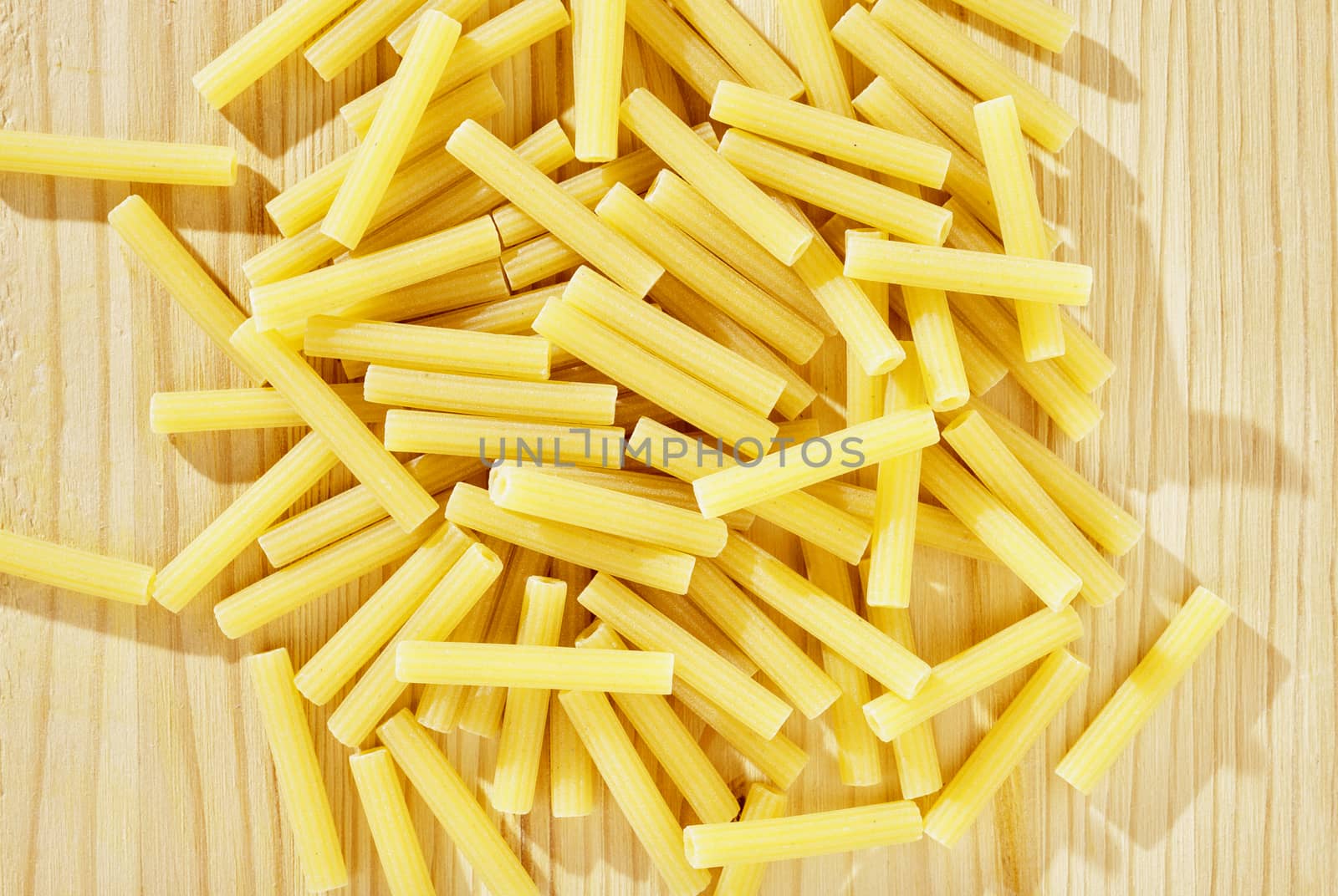 Pile of yellow pasta maccheroni on wooden table , dry pasta shaped like narrow tubes ,