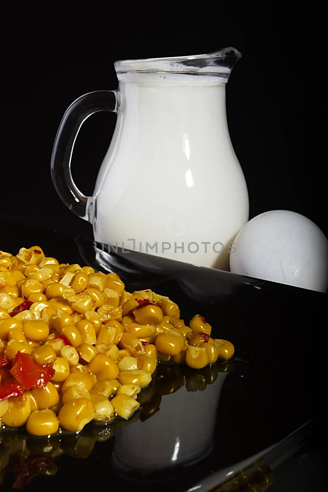 Corn and milk in a jug on a black reflective surface