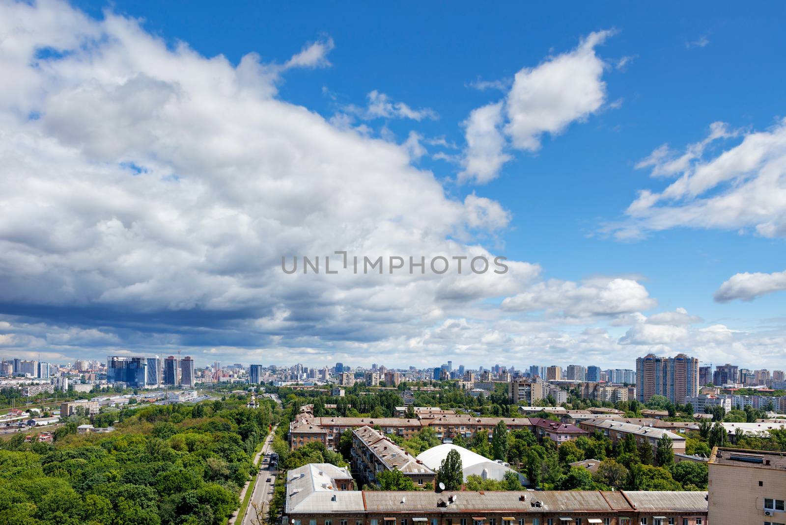 Panoramic view of Kyiv city in summer at noon with a green park in an old residential area and new buildings on the horizon with a blue cloudy sky. Bird's-eye view. Copy space.