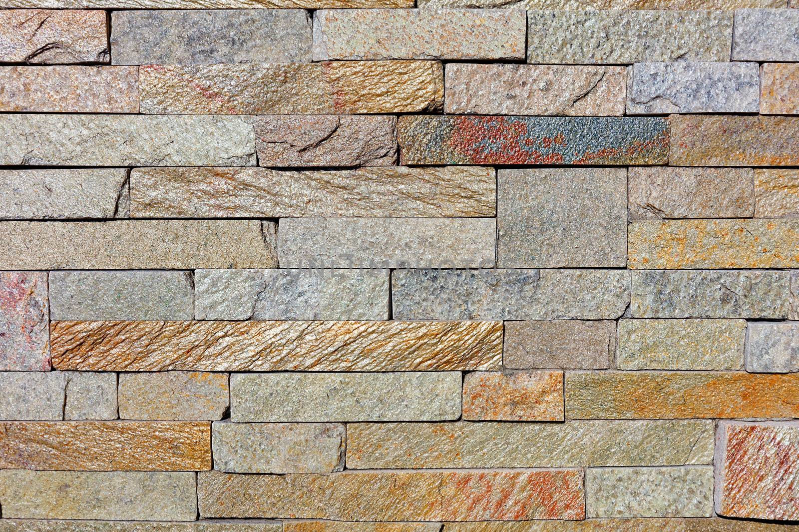 Background and texture of a wall made of shiny, rough, yellow-green sandstone tiles, close-up.
