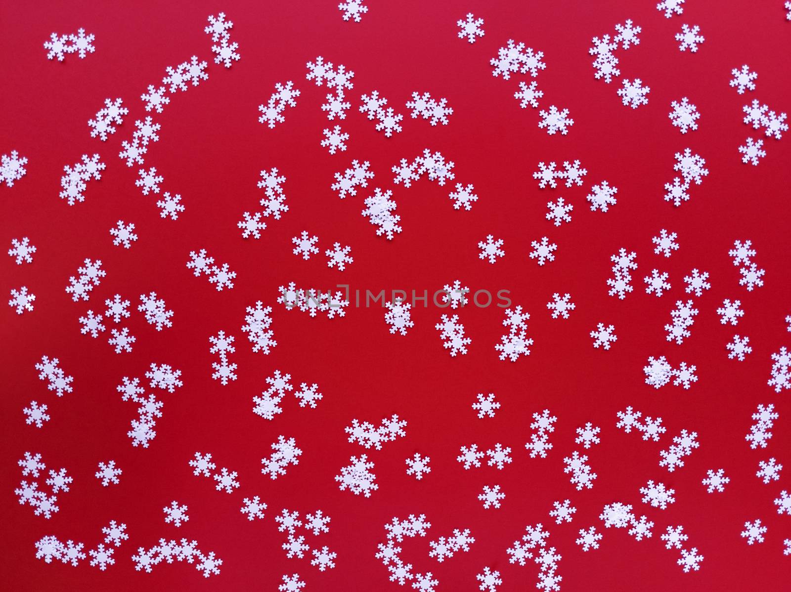 Scattered white snowflakes on red background. Simple festive flat lay. Stock photography.