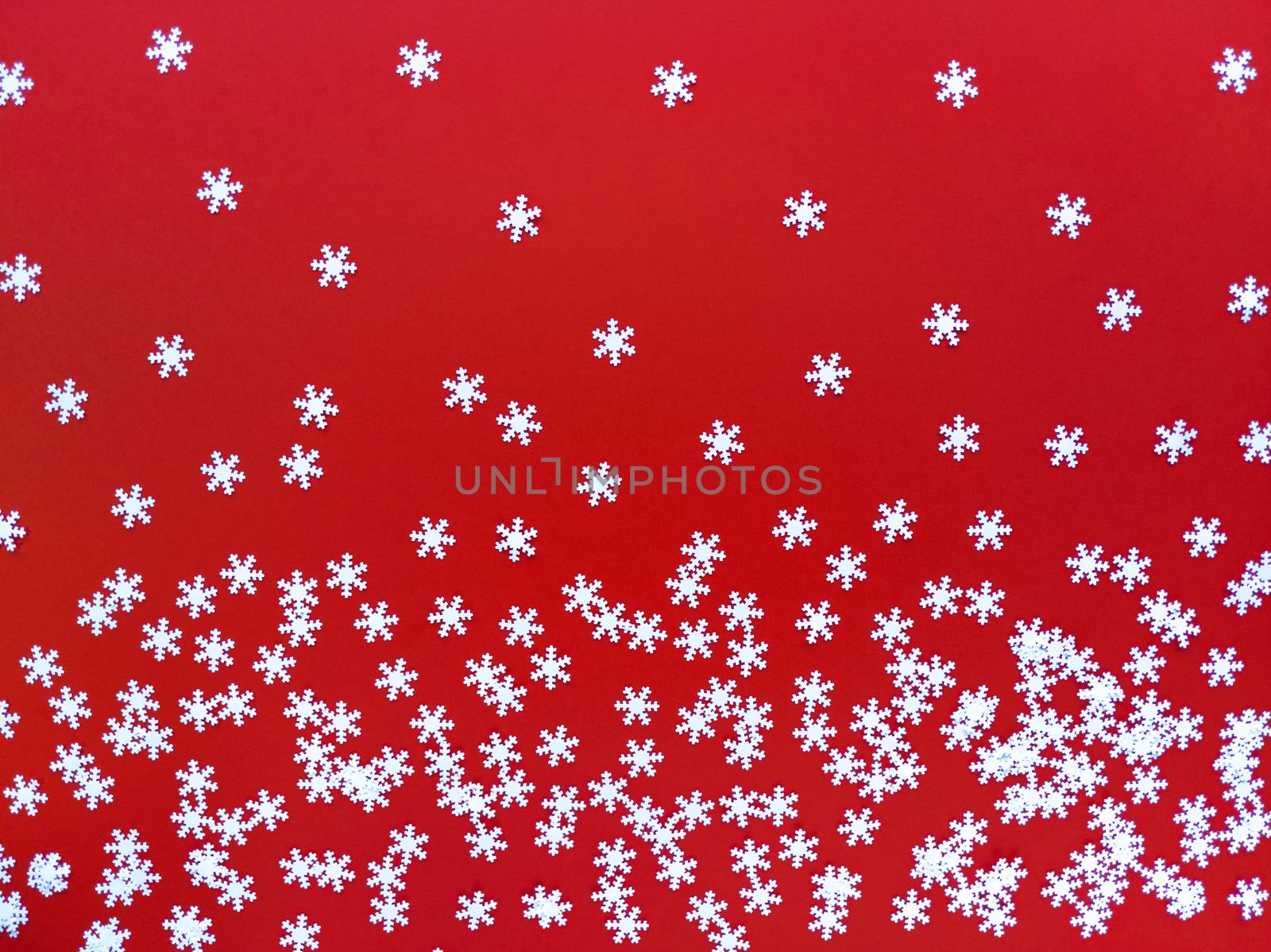 Scattered white snowflakes on red background. Simple festive flat lay. Stock photography.