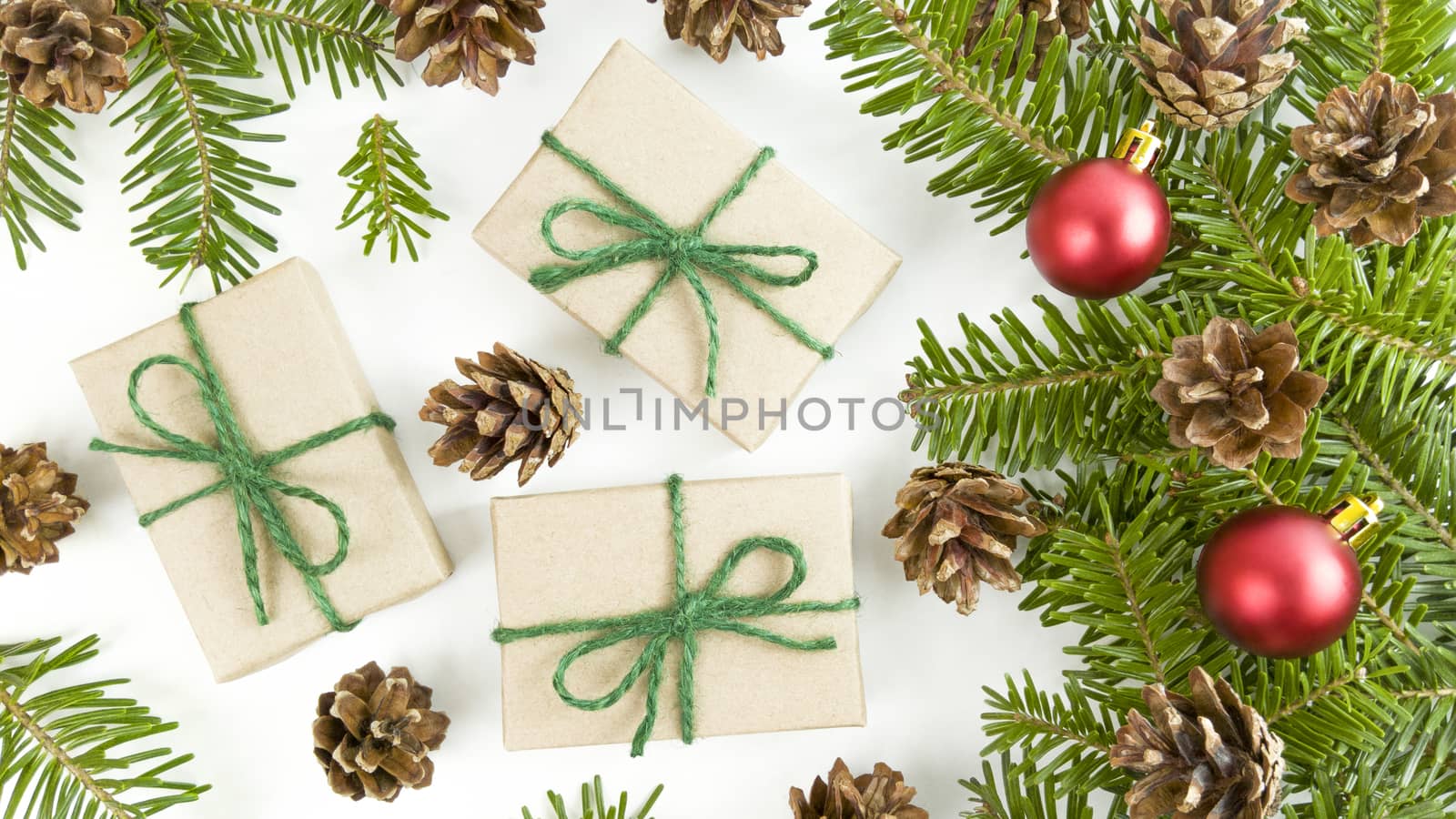 Holiday postcard with craft gift boxes, fir tree branches, cones and red christmas baubles on white background.