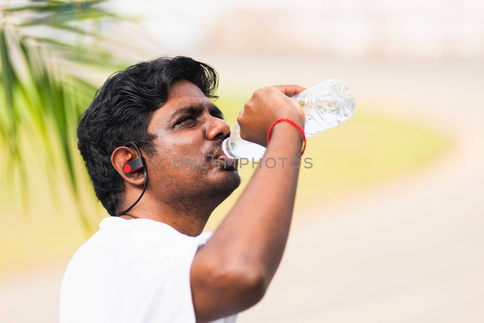 Close up Asian young sport runner black man wear athlete headphones he drinking water from a bottle after running at the outdoor street health park, healthy exercise workout concept