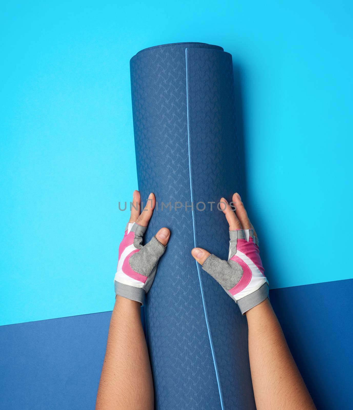 female hand holds a rolled up neoprene sports mat on a blue back by ndanko