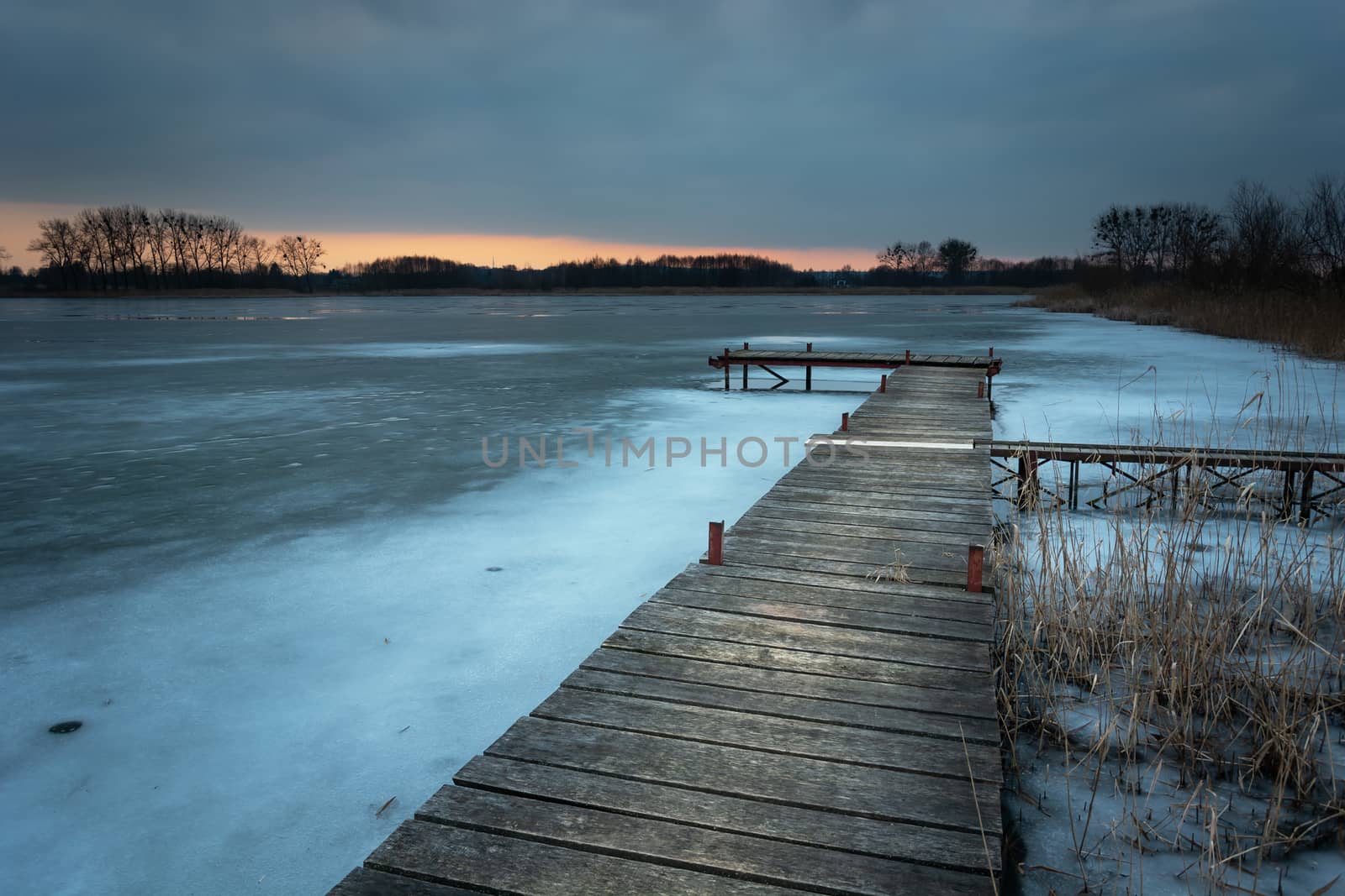 A wooden pier at the shore of a frozen lake, evening view