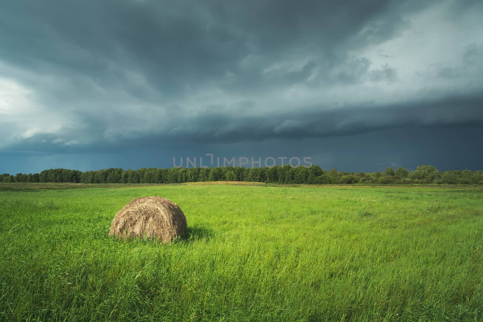 Hay bale on green meadow and dark stormy cloud, summer view