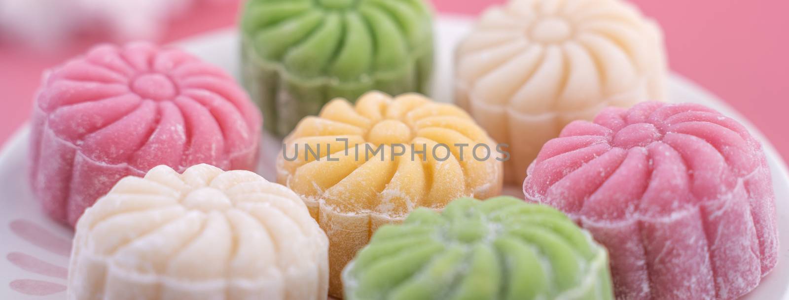 Colorful snow skin moon cake, sweet snowy mooncake, traditional savory dessert for Mid-Autumn Festival on pastel pale pink background, close up.