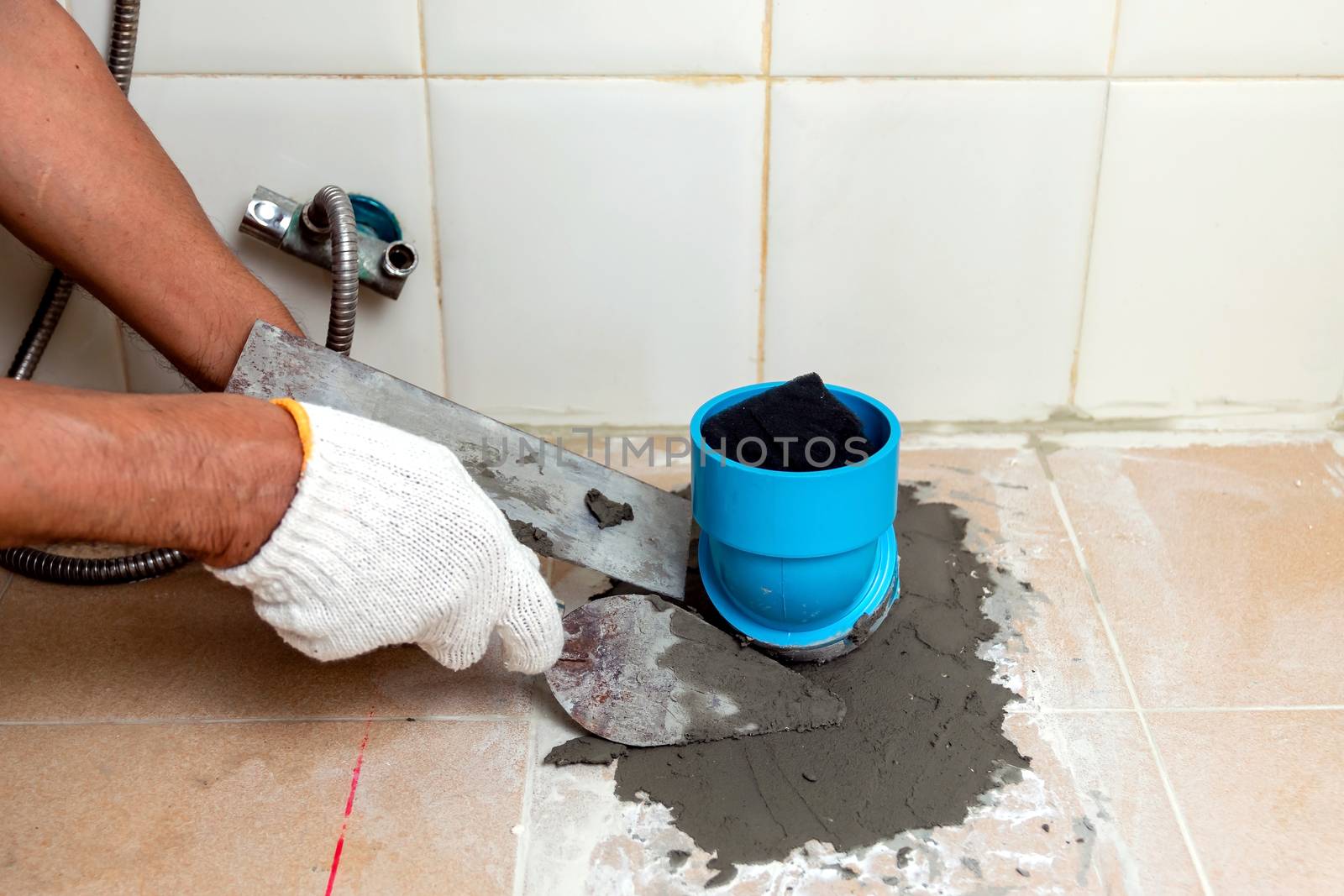 Construction workers are using plastering tools around the PVC pipe to drain the waste inside the bathroom.