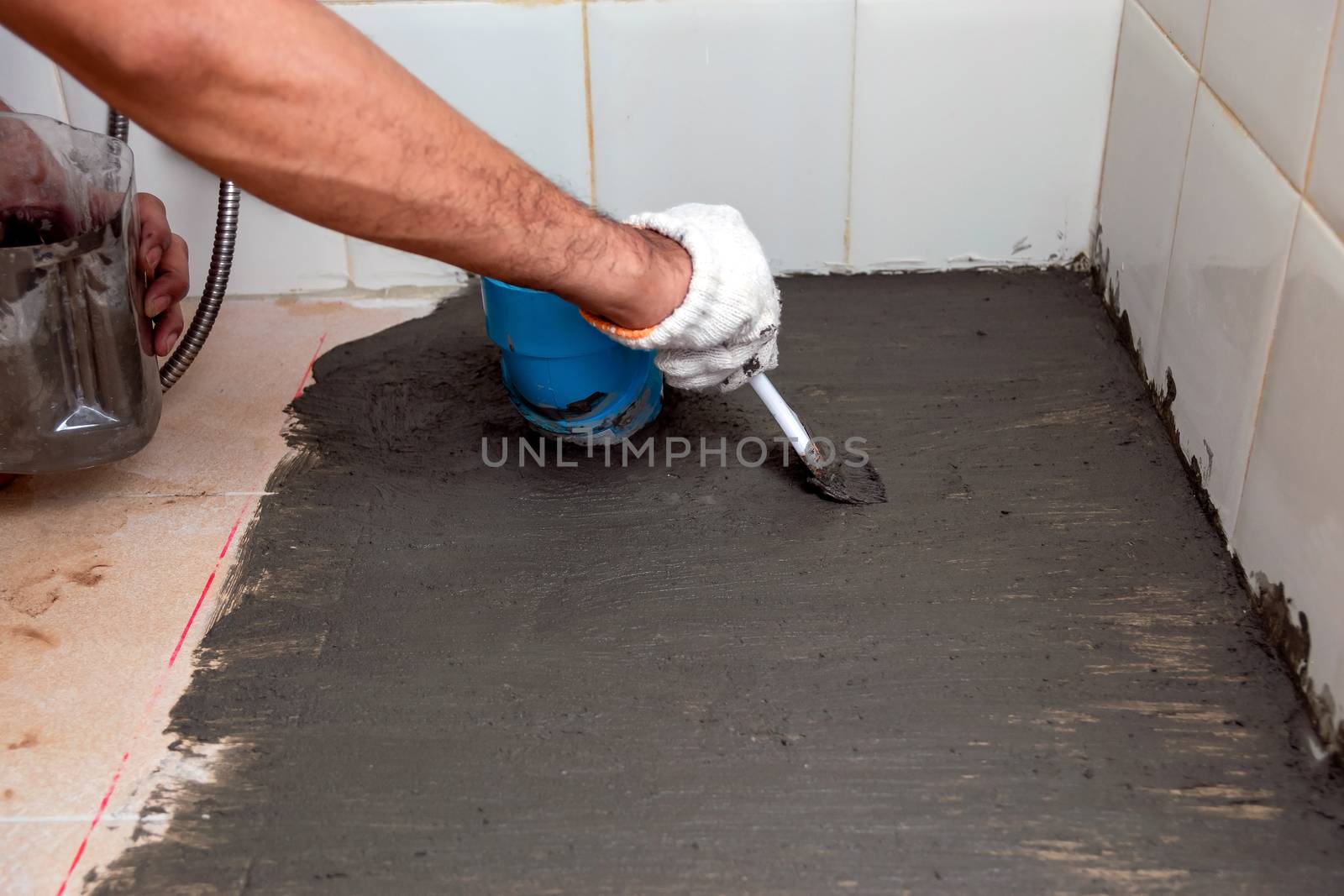 Construction workers are brushing waterproofing cement on tile floors in the bathroom.