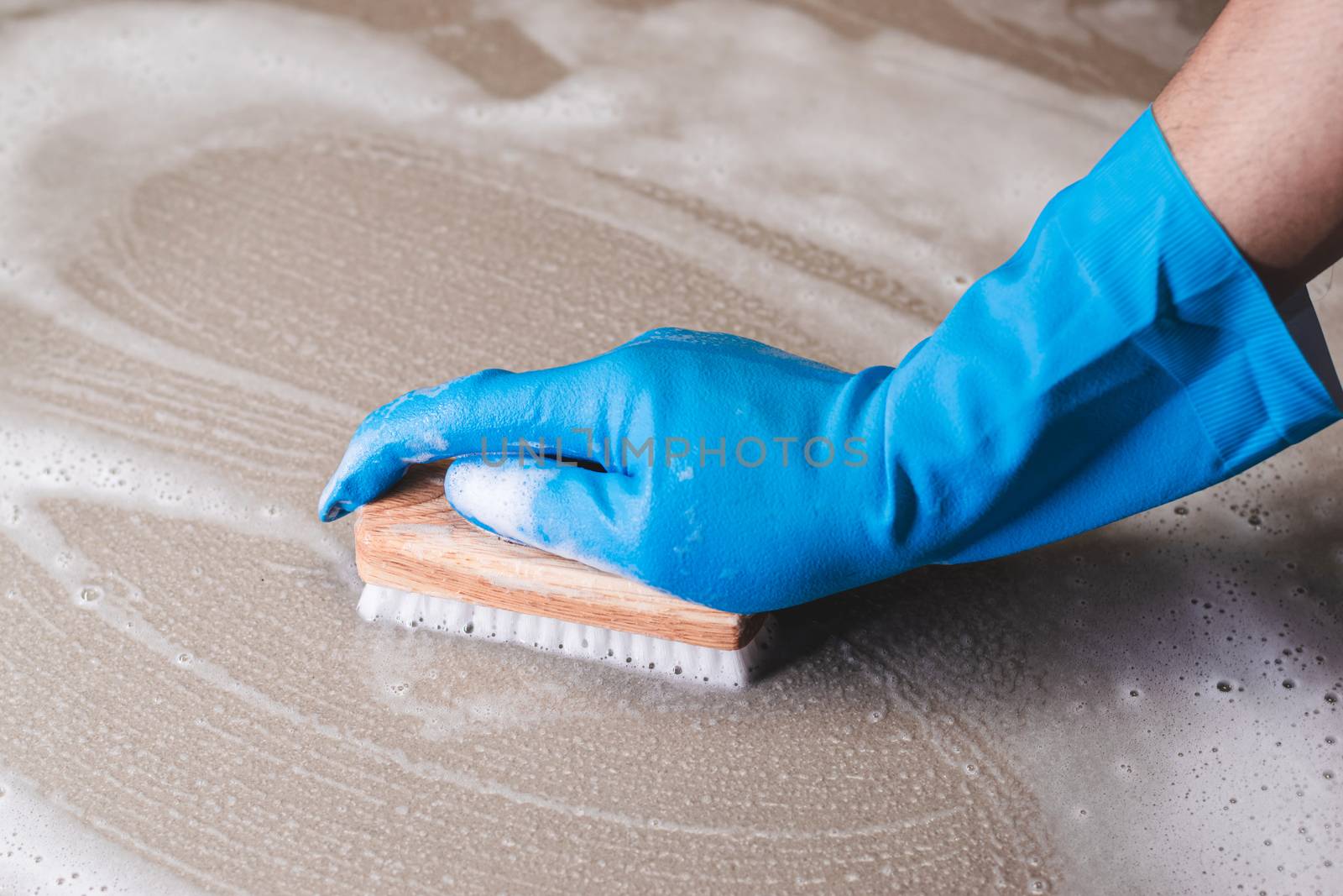 Hand of man wearing blue rubber gloves is used to convert scrub cleaning on the tile floor.