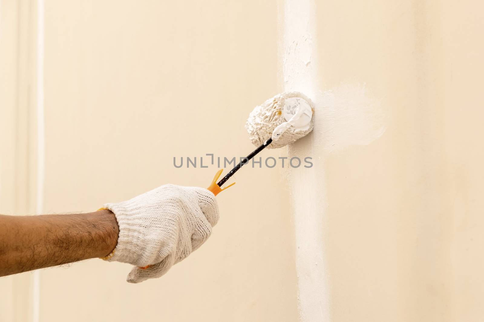 Closeup on hand wearing white cloth gloves, using a roller for painting white color on the concrete wall.