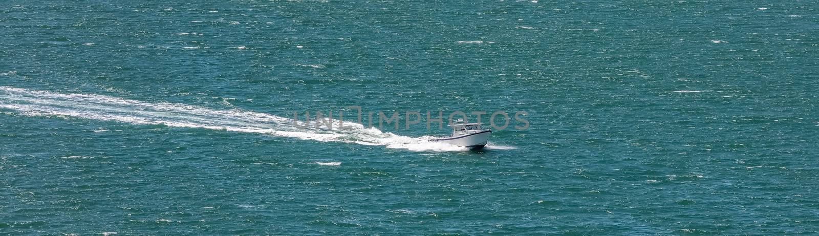 High angle shot of a sailboat sailing in Weymouth Bay, UK. White water trail behind. Panorama size.