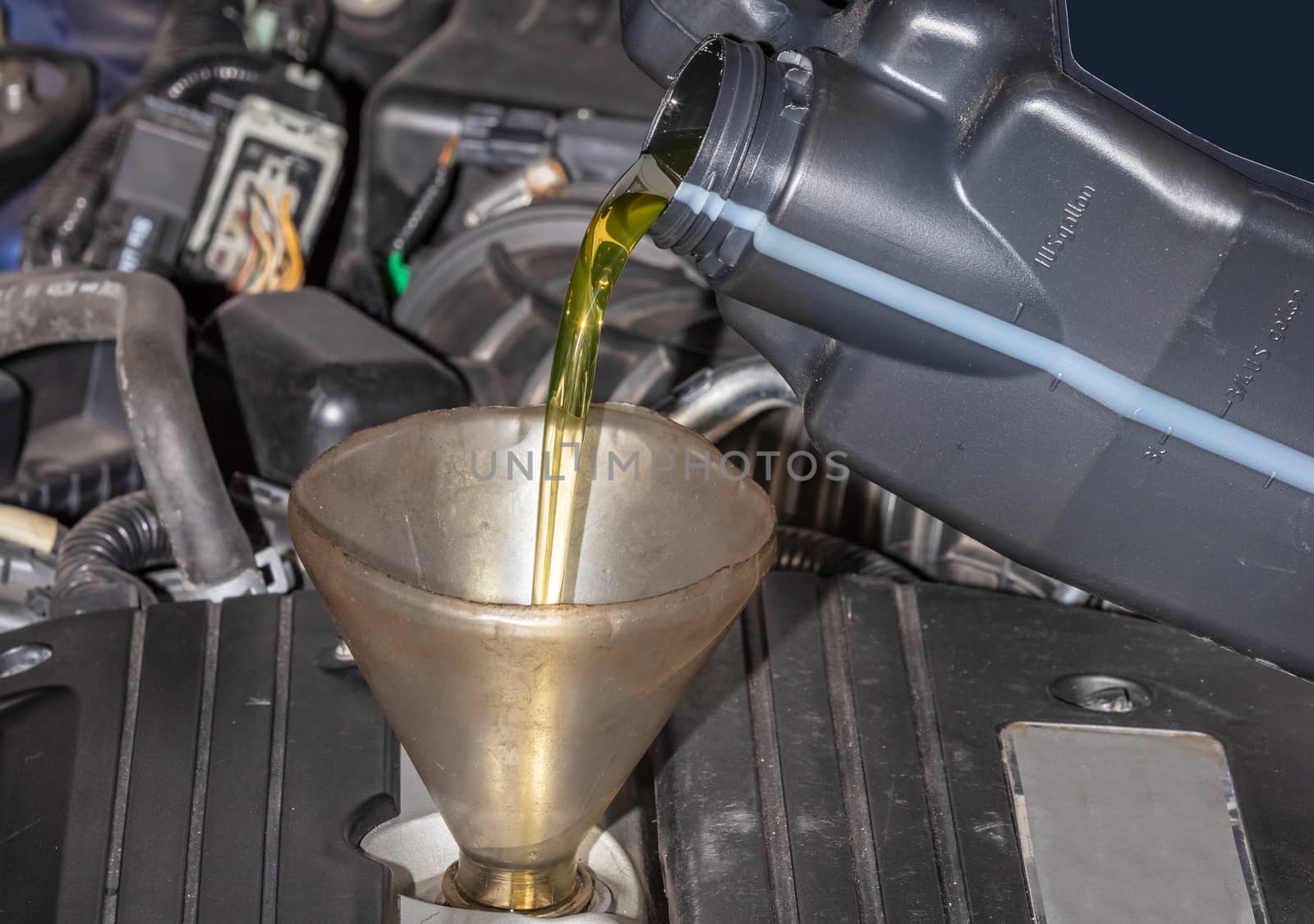 Mechanic topping up the oil in a car pouring a pint of oil through a funnel into the engine, close up of the oil and funnel