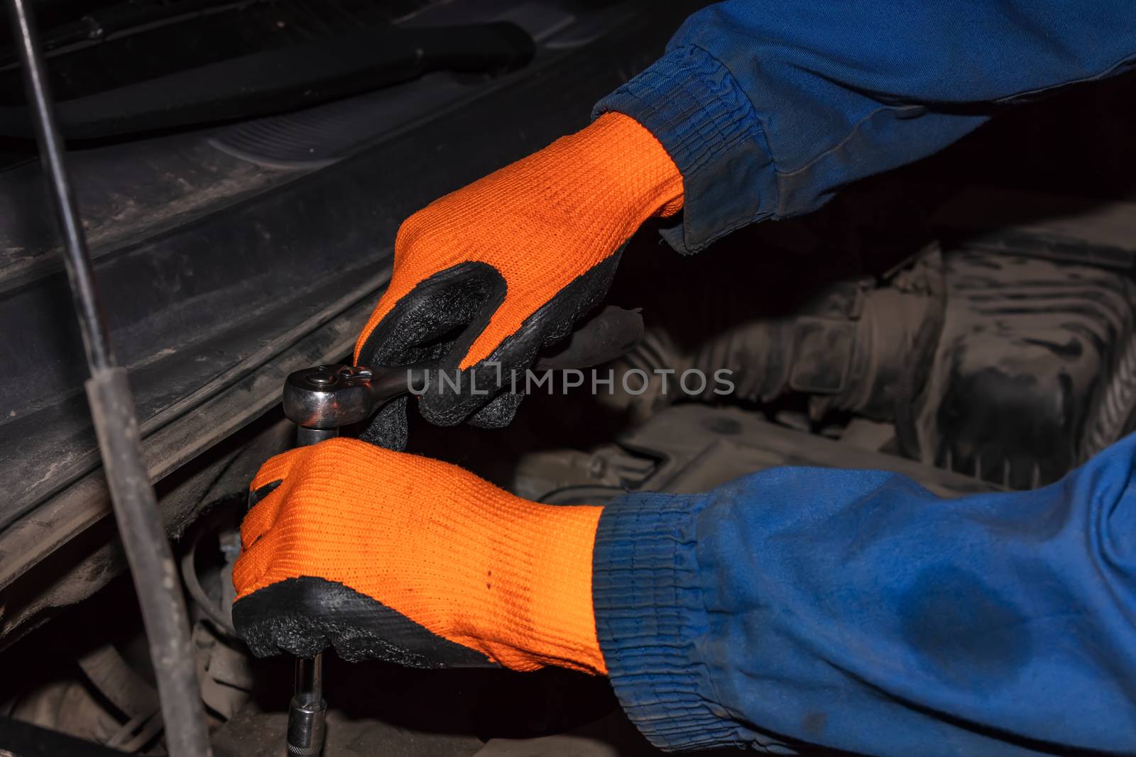 Gloved hands of mechanic holding wrench or spanner working on car engine by DamantisZ